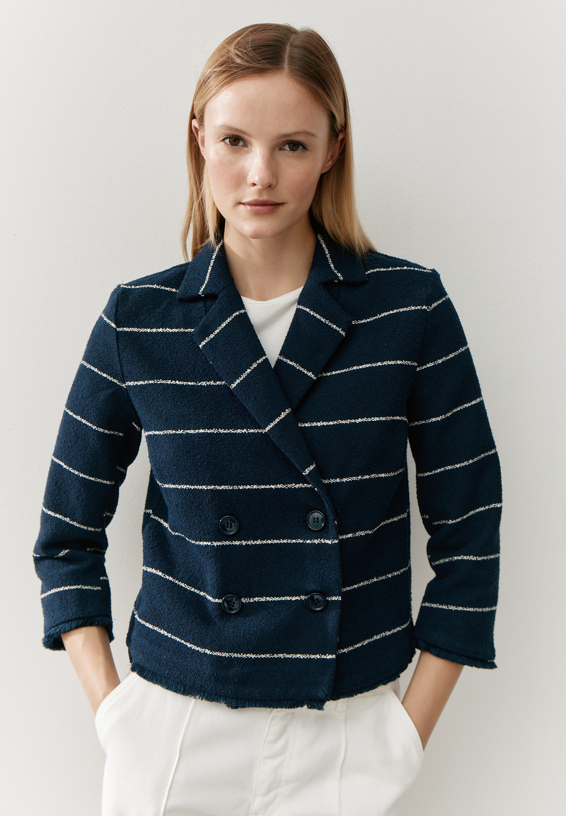 Eine Frau trägt einen blauen Bouclé-Blazer von MORE & MORE mit weißen Streifen.