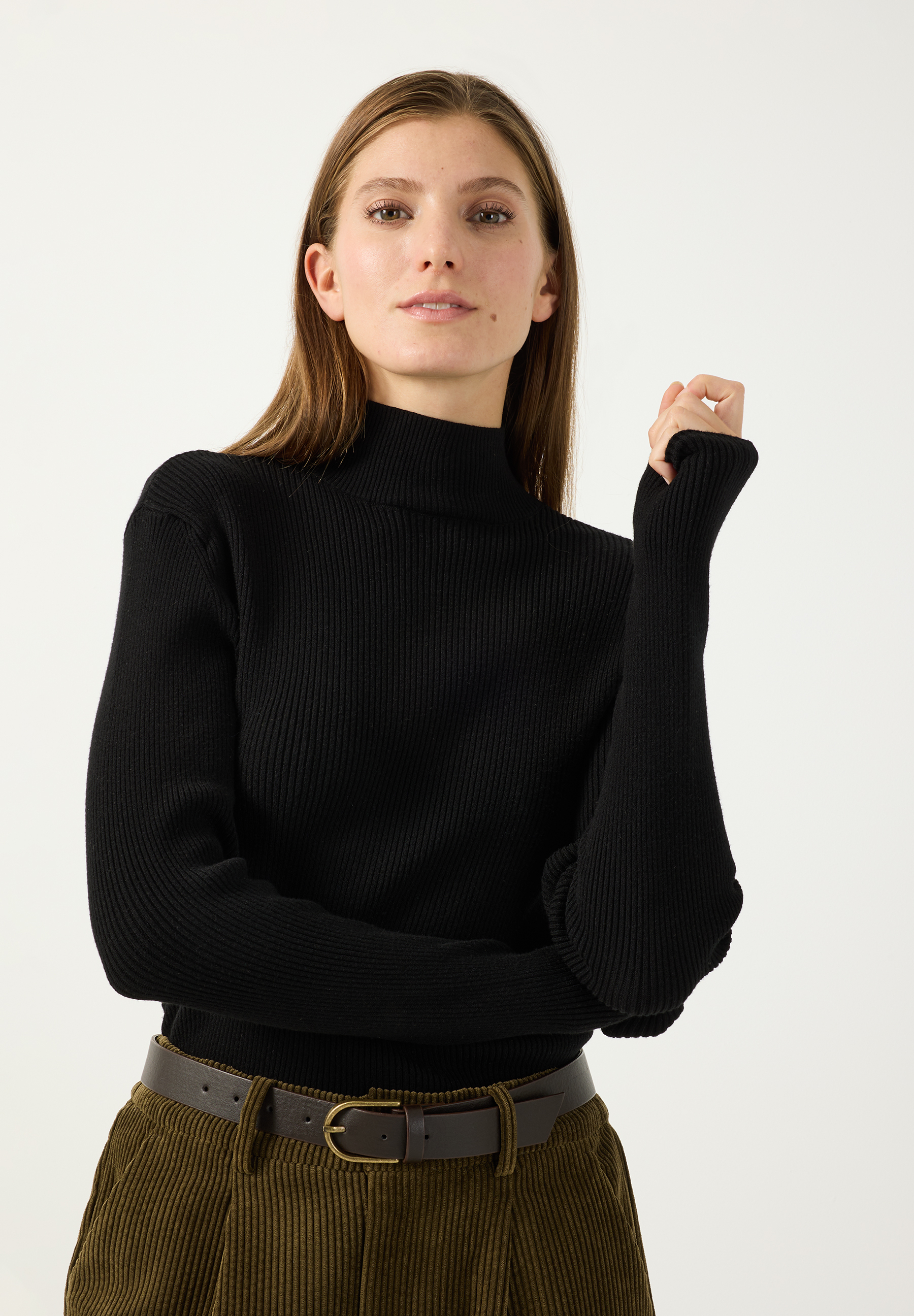 MORE & MORE schwarzer Rollkragenpullover, Modell mit langen Ärmeln mit Bündchen und geripptem Strickmuster. Das Model trägt dazu einen khakifarbenen Cordrock und einen schmalen Gürtel.