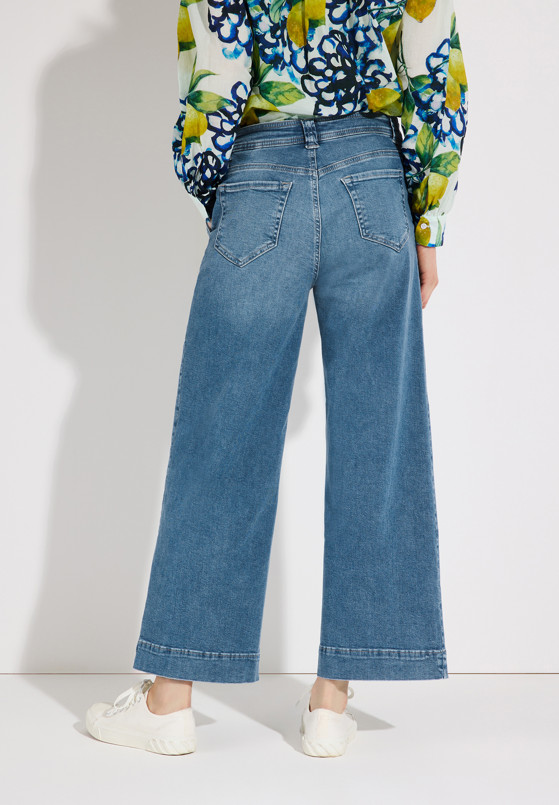 Eine Person trägt MORE & MORE Jeans mit weitem Bein und helle Schuhe vor einer weißen Wand. Eine Person trägt MORE & MORE Jeans mit weitem Bein und helle Schuhe vor einer weißen Wand.