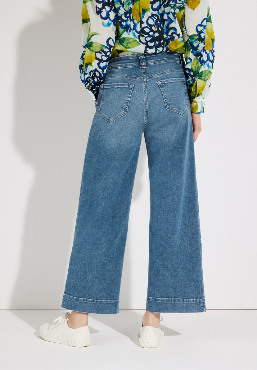 Eine Person trägt MORE & MORE Jeans mit weitem Bein und helle Schuhe vor einer weißen Wand. Eine Person trägt MORE & MORE Jeans mit weitem Bein und helle Schuhe vor einer weißen Wand.