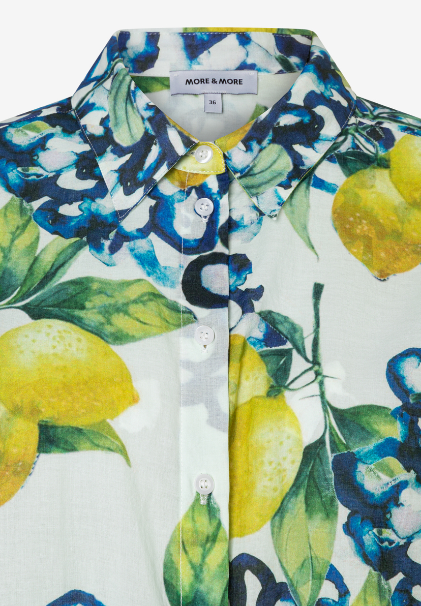 Nahaufnahme einer MORE & MORE Bluse mit Zitronen- und Blumenmuster, Knöpfen und Etikett. Nahaufnahme einer MORE & MORE Bluse mit Zitronen- und Blumenmuster, Knöpfen und Etikett.