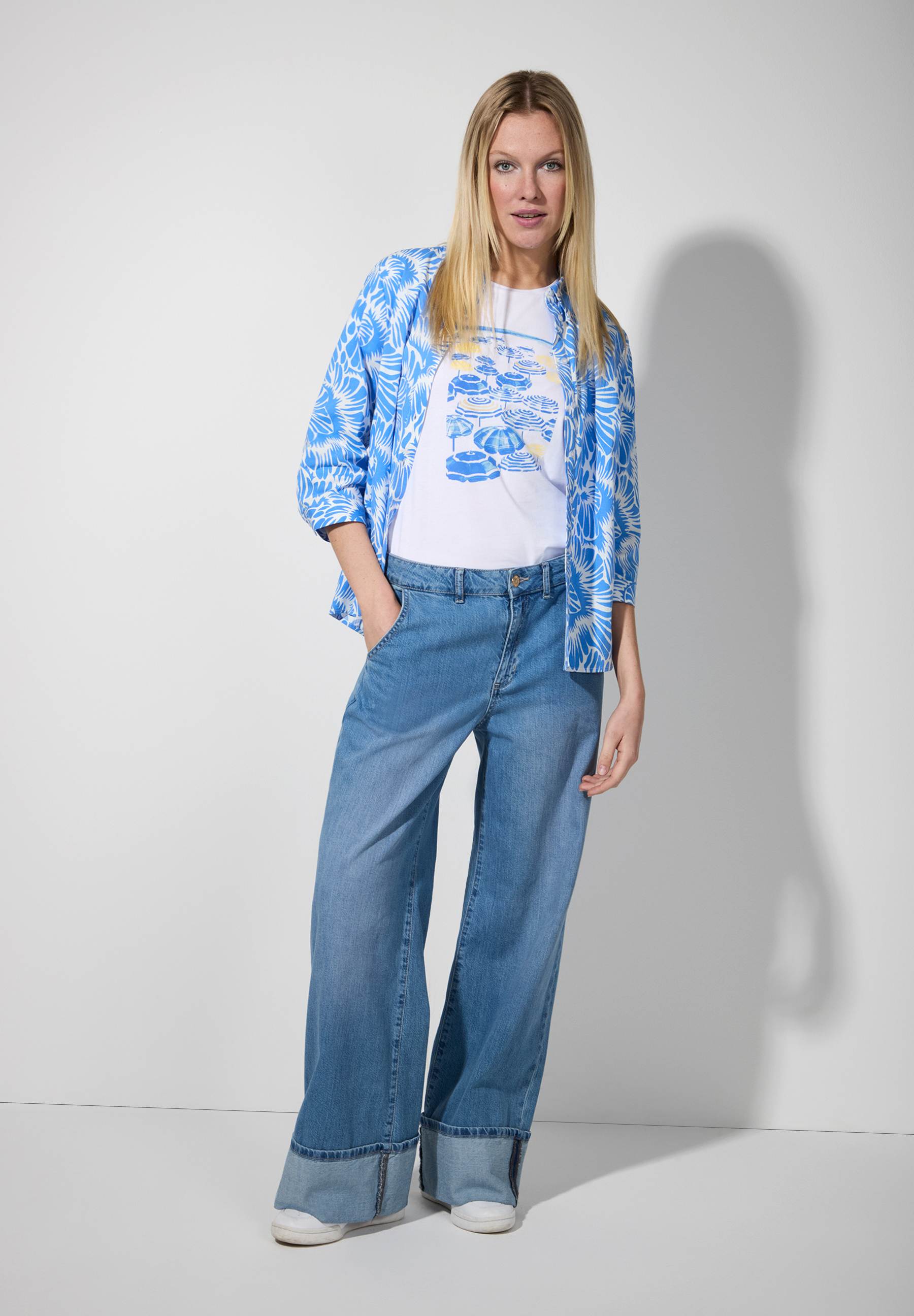 Eine Frau in MORE & MORE Oberteilen mit blau-weiß gemusterter Bluse und Jeans. Eine Frau in MORE & MORE Oberteilen mit blau-weiß gemusterter Bluse und Jeans.