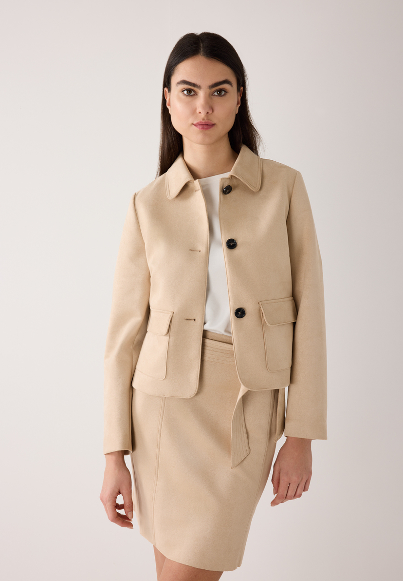 Eine Frau mit MORE & MORE Blazer aus Kunstleder und passendem Rock vor hellem Hintergrund. Eine Frau mit MORE & MORE Blazer aus Kunstleder und passendem Rock vor hellem Hintergrund.