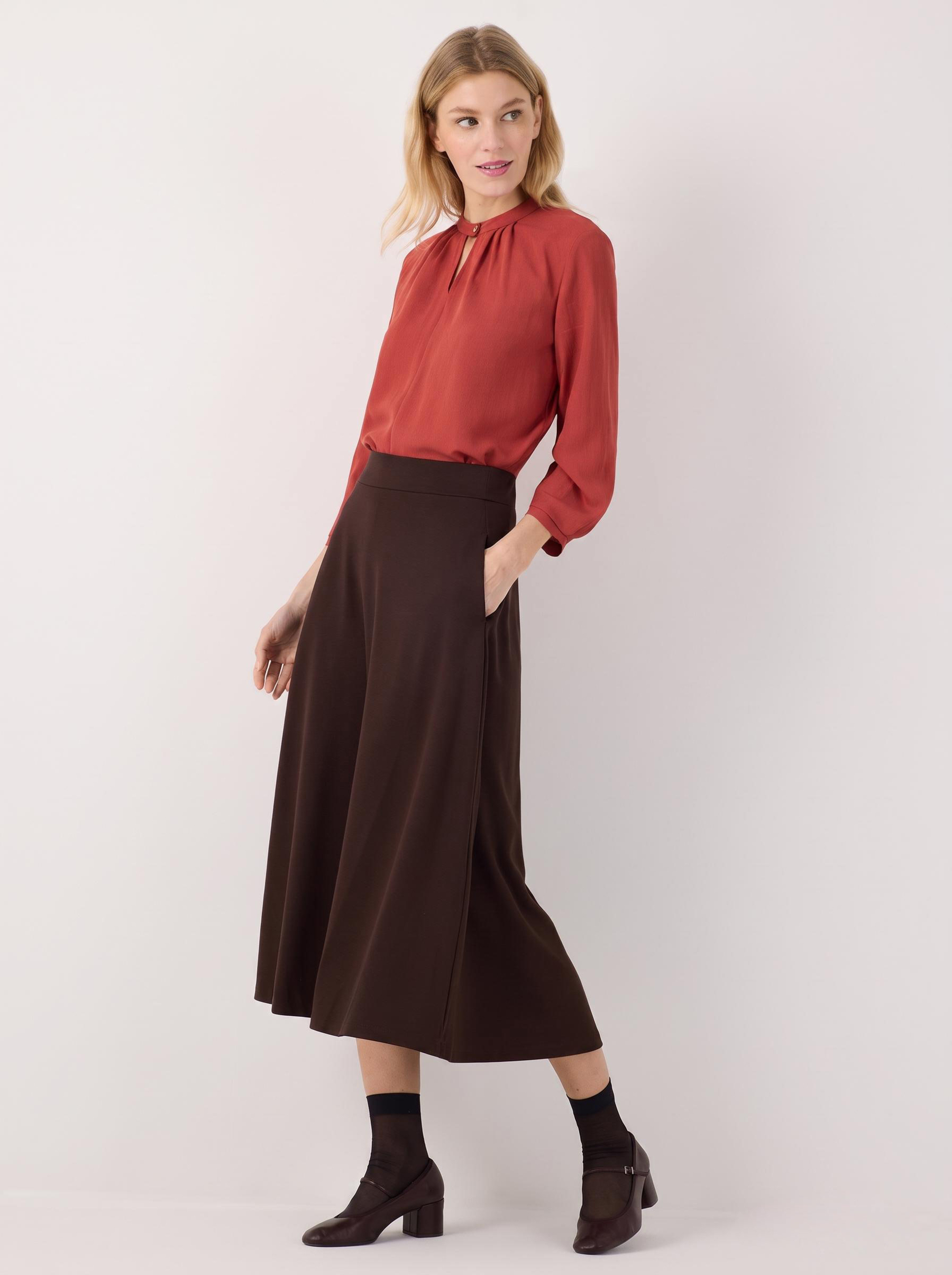 MORE & MORE Bluse aus fließendem Jersey in Rostrot mit Stehkragen und geraffter Brustpartie, kombiniert mit dunklem Rock.