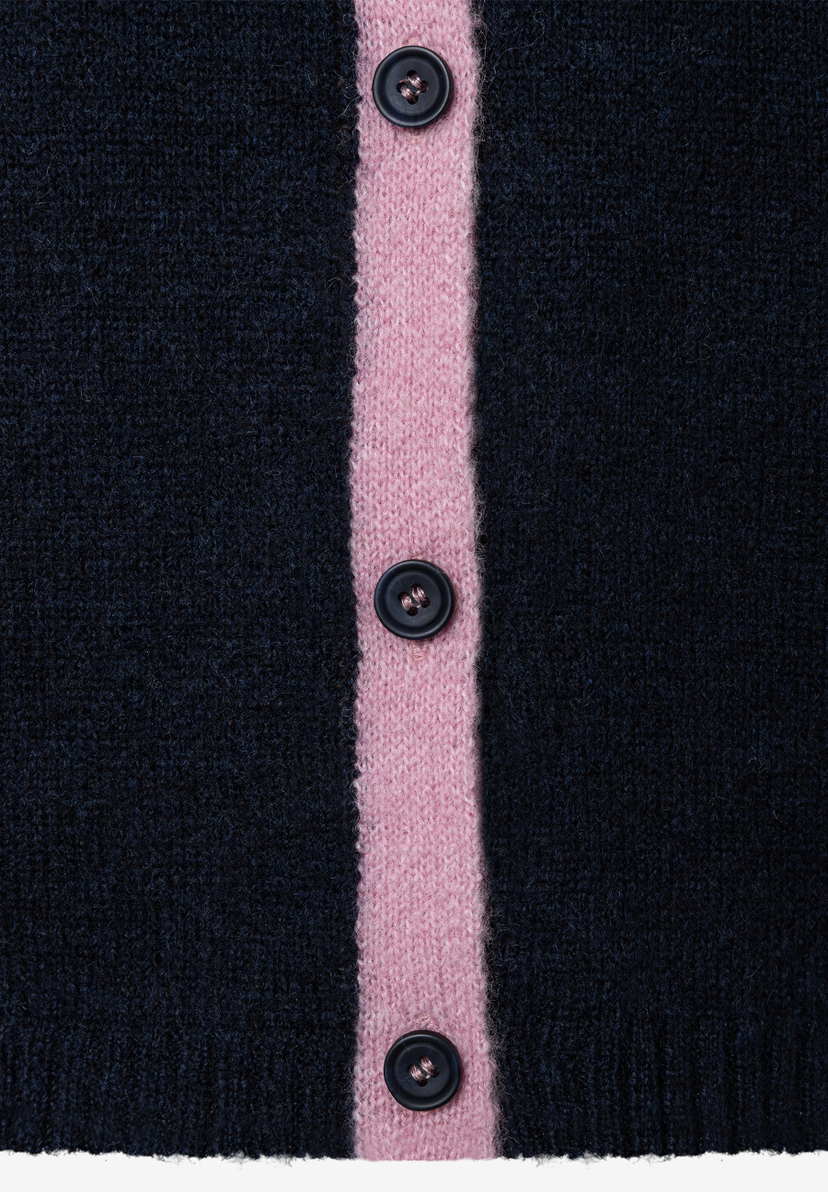 MORE & MORE Pullover & Strickwaren: Nahaufnahme einer dunkelblauen Strickjacke mit einem rosa Streifen in der Mitte und drei dunklen Knöpfen. MORE & MORE Pullover & Strickwaren: Nahaufnahme einer dunkelblauen Strickjacke mit einem rosa Streifen in der Mitte und drei dunklen Knöpfen.