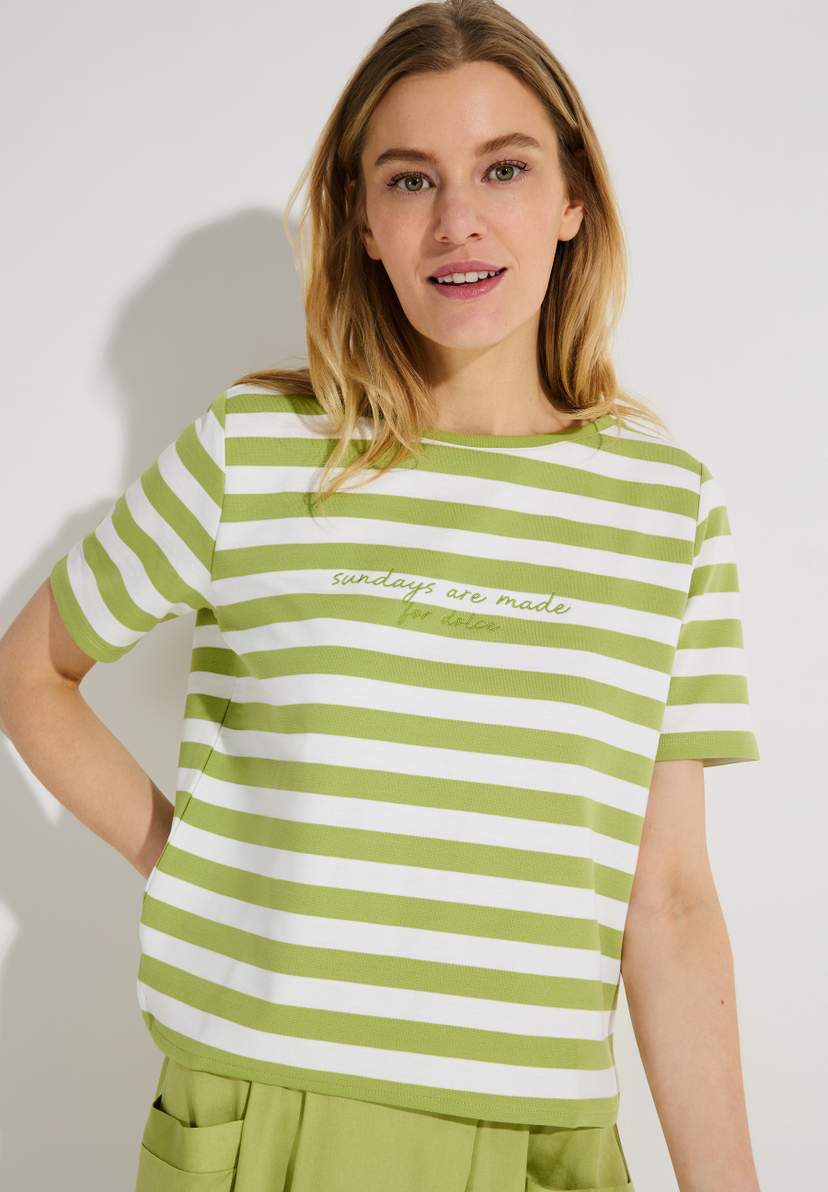 Eine Frau trägt ein MORE & MORE Jersey-Top mit grünen und weißen Streifen und der Aufschrift "Sundays are made for dolce". Eine Frau trägt ein MORE & MORE Jersey-Top mit grünen und weißen Streifen und der Aufschrift "Sundays are made for dolce".