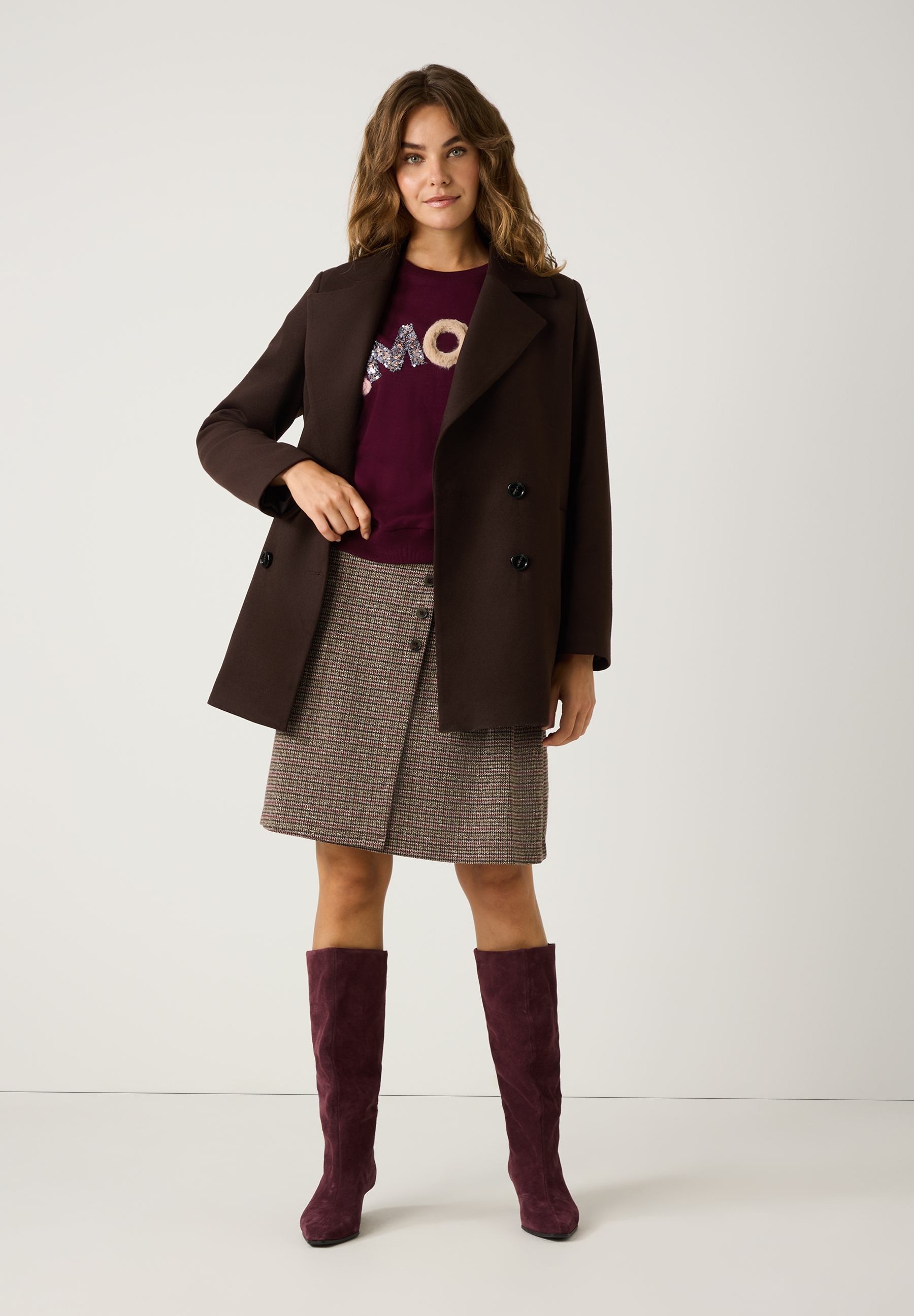 Eine Frau in MORE & MORE Oberteilen: braunem Kurzmantel, bordeauxrotem Shirt und Rock. Dazu farblich passende Stiefel. Eine Frau in MORE & MORE Oberteilen: braunem Kurzmantel, bordeauxrotem Shirt und Rock. Dazu farblich passende Stiefel.