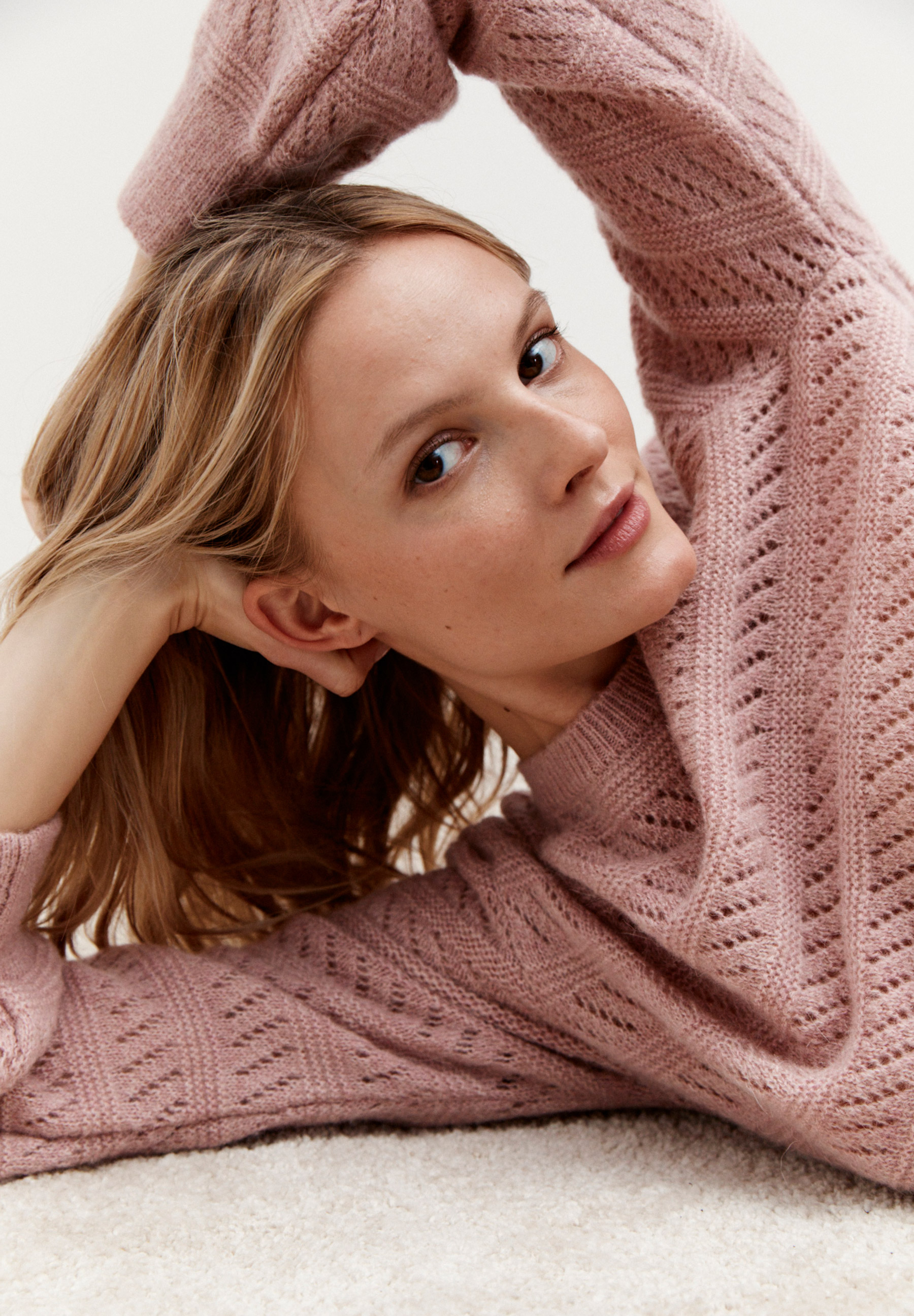 Eine Frau trägt einen rosafarbenen Strukturstrick-Pullover von MORE & MORE und blickt in die Kamera. Eine Frau trägt einen rosafarbenen Strukturstrick-Pullover von MORE & MORE und blickt in die Kamera.