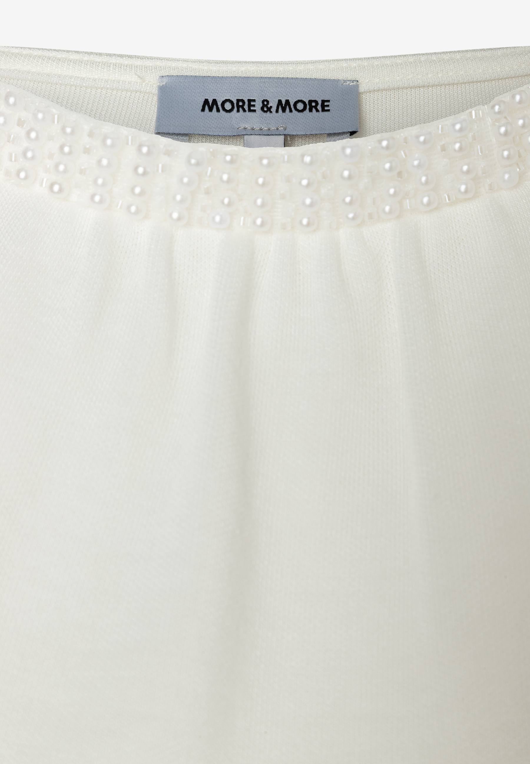 Detailansicht eines MORE & MORE Oberteils mit Jersey-Material und Perlenbesatz am Kragen. Detailansicht eines MORE & MORE Oberteils mit Jersey-Material und Perlenbesatz am Kragen.