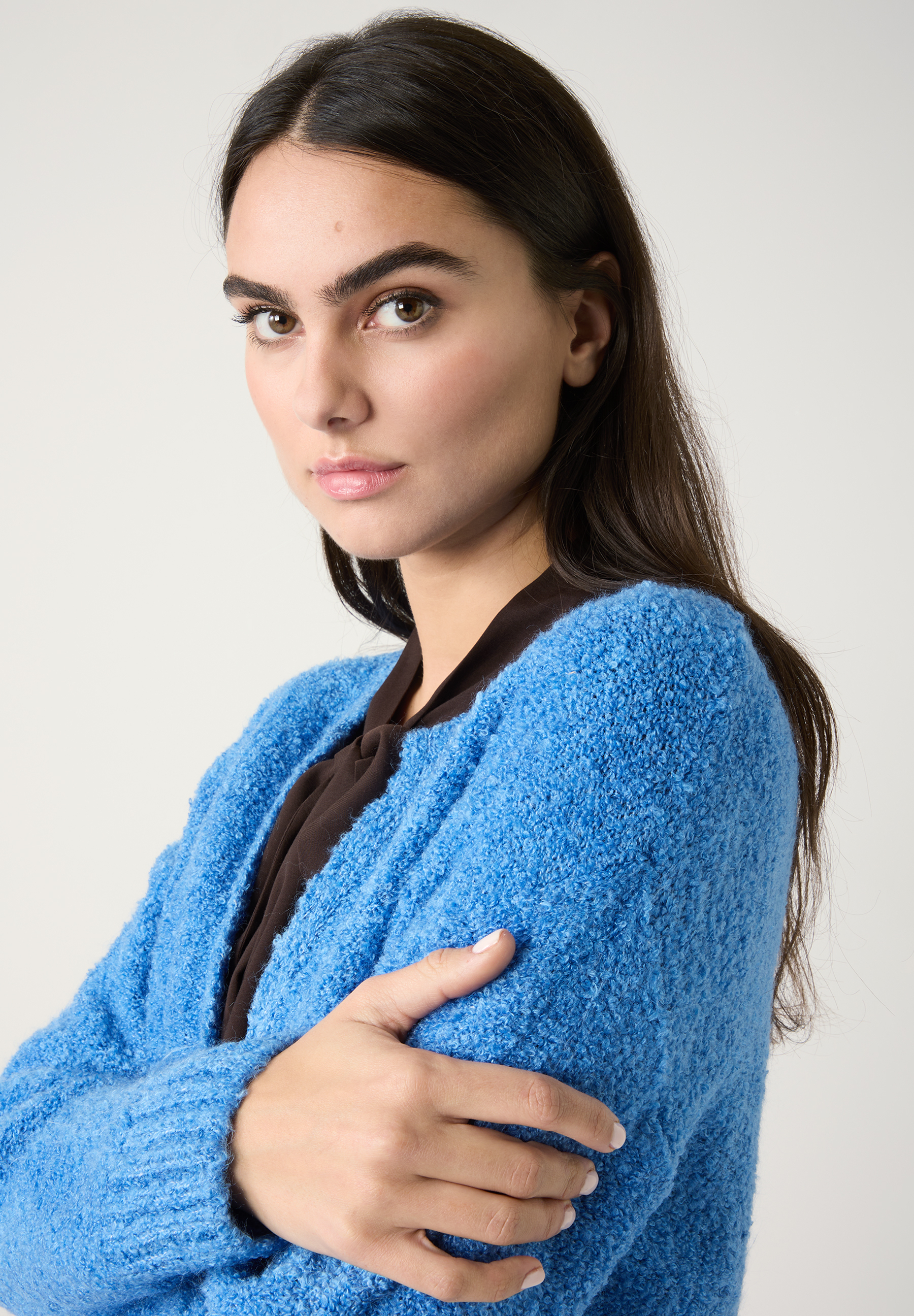 Eine Frau mit einem blauen MORE & MORE Strickoberteil und verschränkten Armen blickt in die Kamera. Eine Frau mit einem blauen MORE & MORE Strickoberteil und verschränkten Armen blickt in die Kamera.