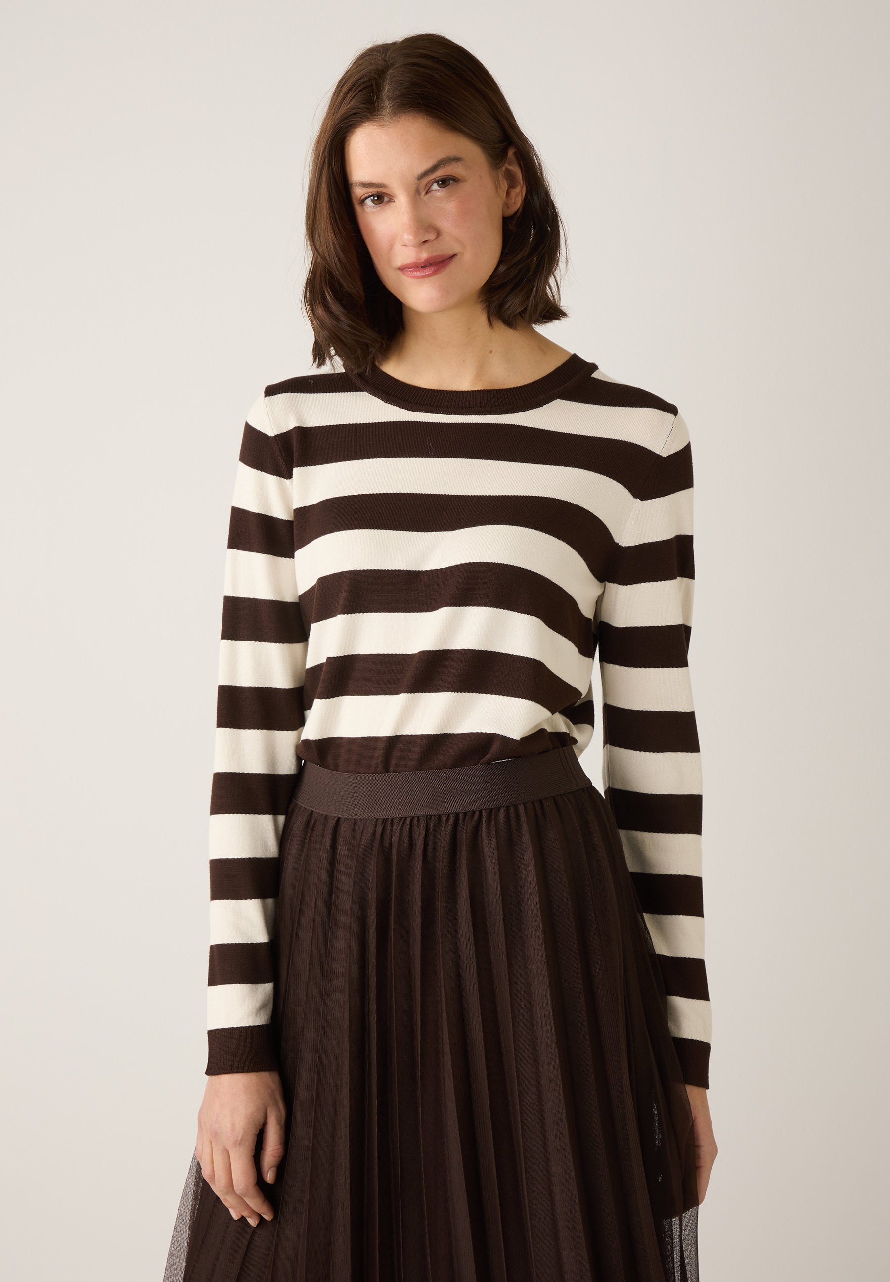 Eine Frau mit MORE & MORE Oberteil/Pullover mit braun-weißen Streifen und einem braunen Rock. Eine Frau mit MORE & MORE Oberteil/Pullover mit braun-weißen Streifen und einem braunen Rock.