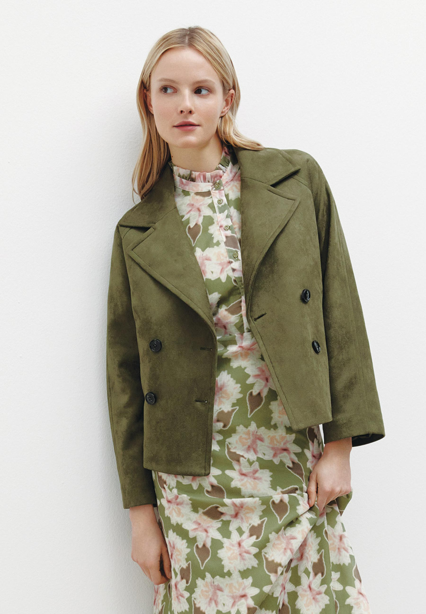 Eine Frau trägt einen MORE & MORE Kunstleder-Blazer über einem grün-rosa geblümten Kleid.
