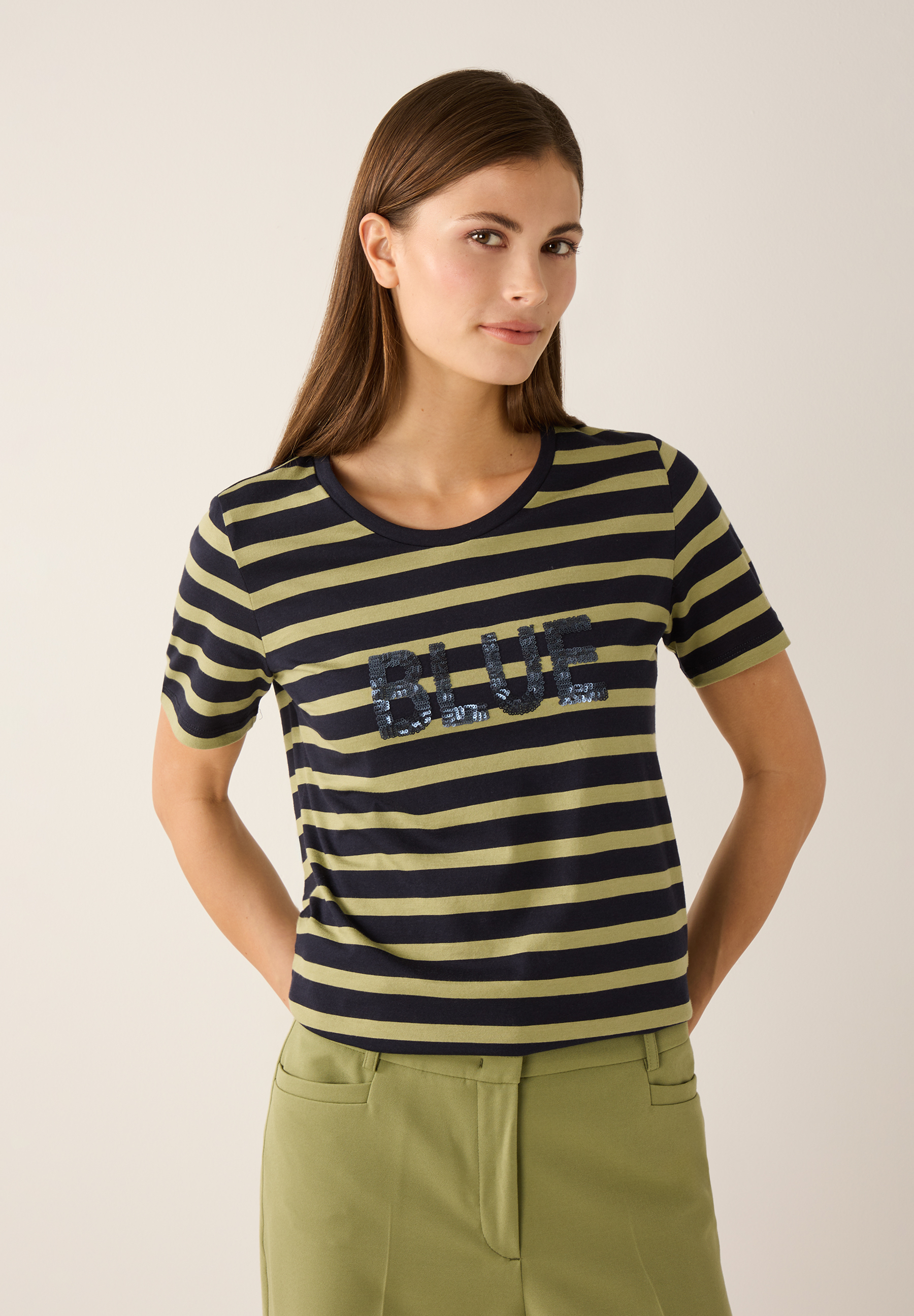 Eine Frau trägt ein gestreiftes MORE & MORE T-Shirt mit "BLUE"-Aufschrift. Eine Frau trägt ein gestreiftes MORE & MORE T-Shirt mit "BLUE"-Aufschrift.