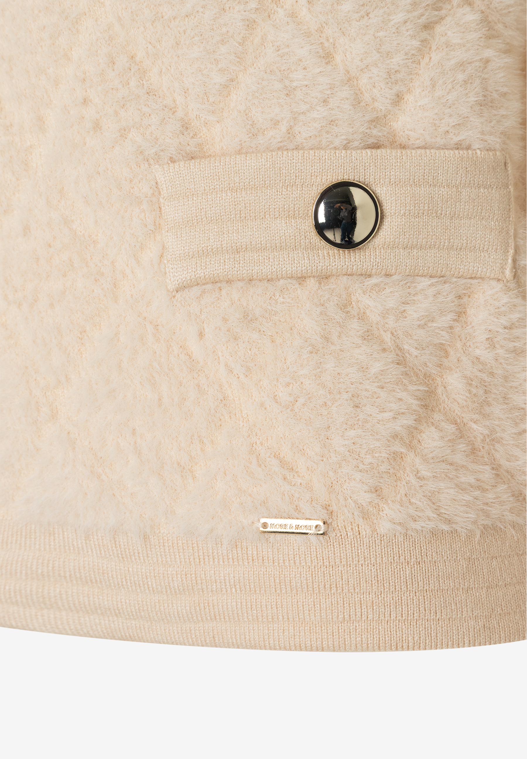 Detailansicht eines MORE & MORE Oberteils aus Kunstfell mit Knopf und Logo. Detailansicht eines MORE & MORE Oberteils aus Kunstfell mit Knopf und Logo.