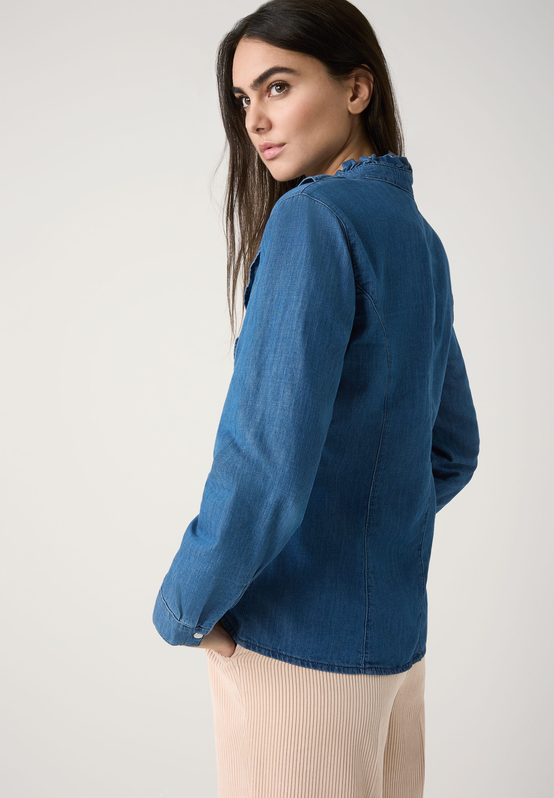 Eine Frau mit braunen Haaren trägt eine blaue MORE & MORE Bluse. Oberteil mit Kräuseldetails am Kragen. Eine Frau mit braunen Haaren trägt eine blaue MORE & MORE Bluse. Oberteil mit Kräuseldetails am Kragen.