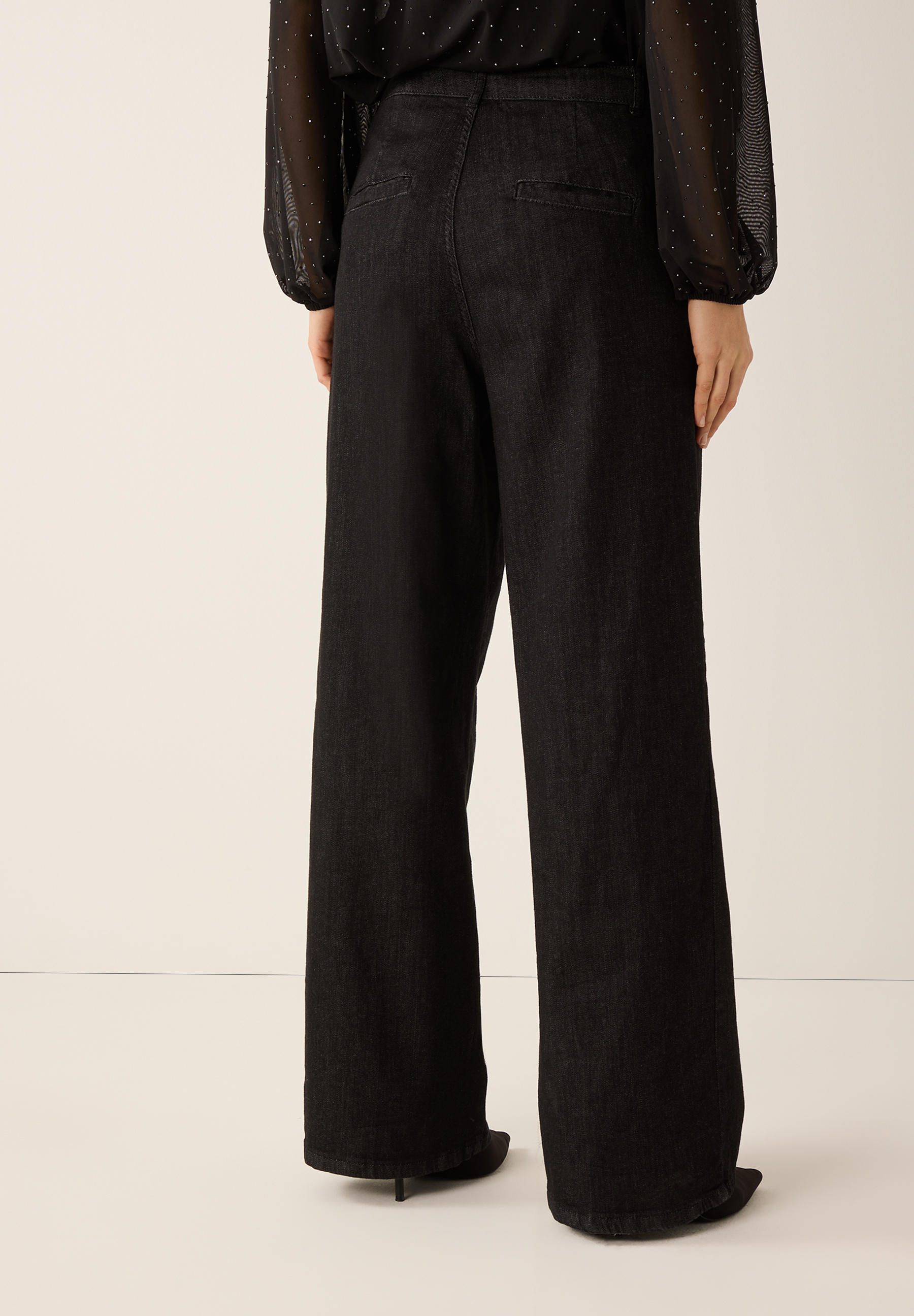 Eine Person trägt MORE & MORE Jeans aus dunklem Denim mit weitem Bein und hoher Taille. Eine Person trägt MORE & MORE Jeans aus dunklem Denim mit weitem Bein und hoher Taille.
