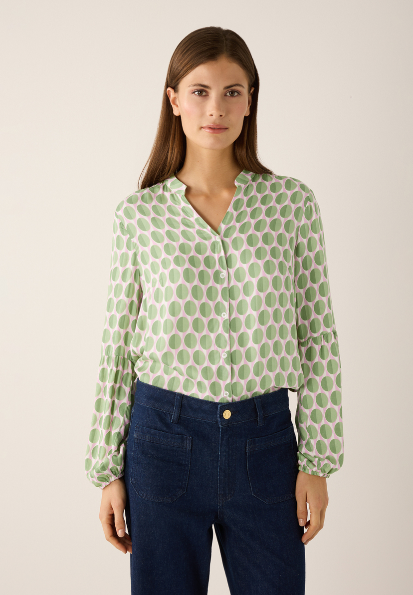 Eine Frau trägt eine grüne MORE & MORE Bluse mit rosafarbenen Punkten und Jeans. Eine Frau trägt eine grüne MORE & MORE Bluse mit rosafarbenen Punkten und Jeans.