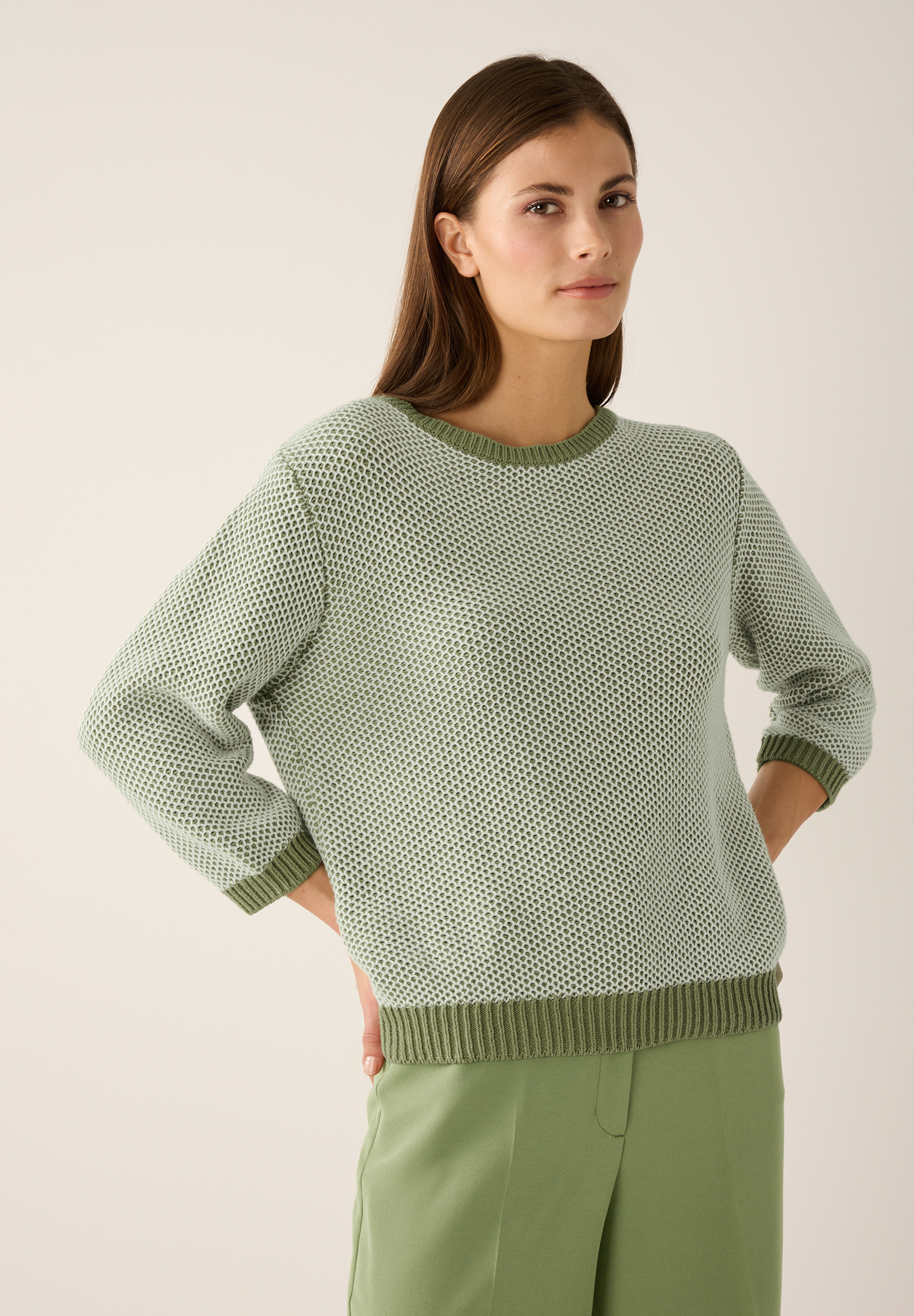 Eine Frau mit einem MORE & MORE Strukturstrick-Pullover in Grün posiert.