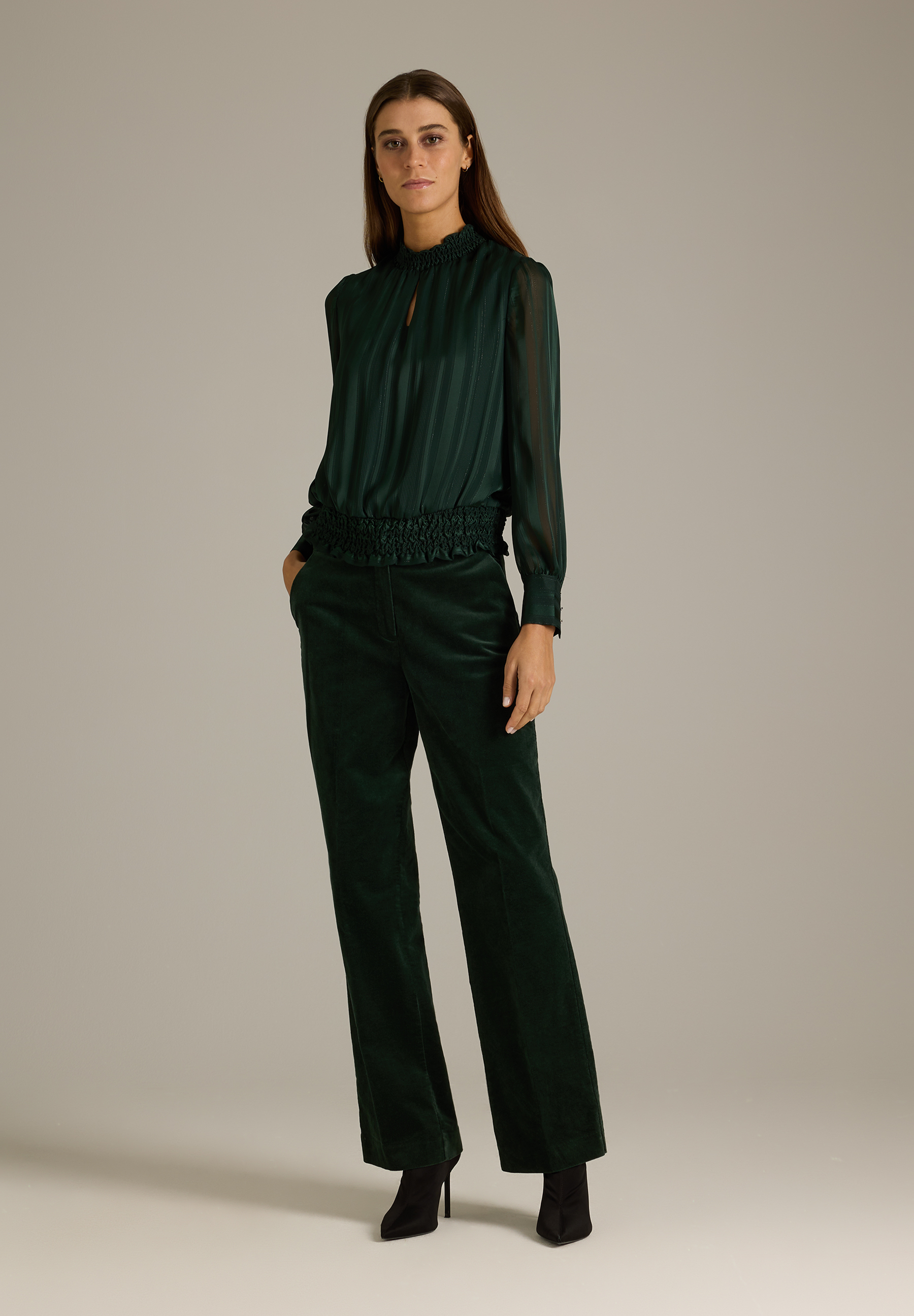 MORE & MORE Bluse: Eine Frau trägt eine dunkelgrüne, hochgeschlossene Langarmbluse und eine passende Hose. MORE & MORE Bluse: Eine Frau trägt eine dunkelgrüne, hochgeschlossene Langarmbluse und eine passende Hose.