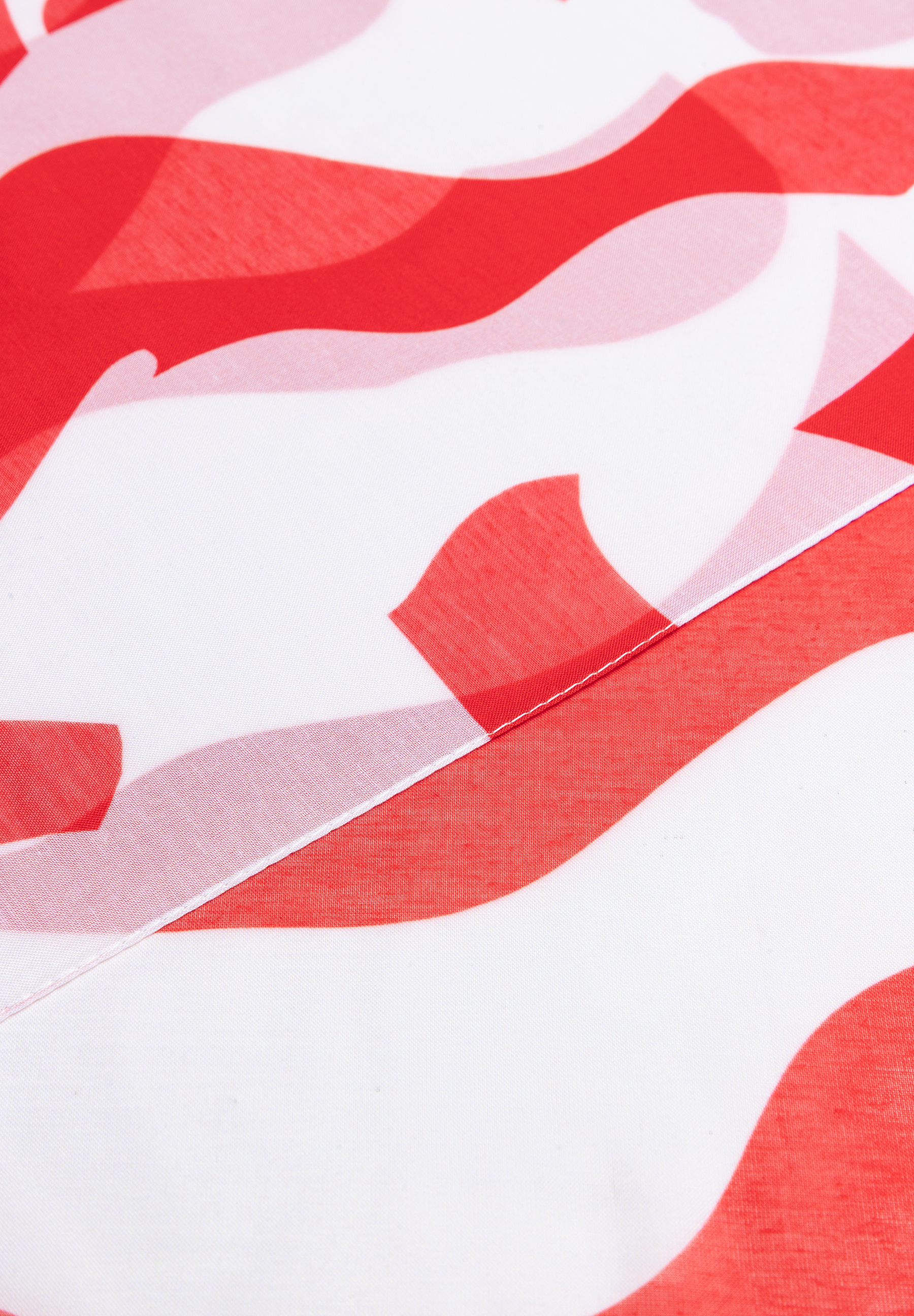 Nahaufnahme eines MORE & MORE Accessoires mit abstraktem, rotem Muster auf weißem Grund. Nahaufnahme eines MORE & MORE Accessoires mit abstraktem, rotem Muster auf weißem Grund.