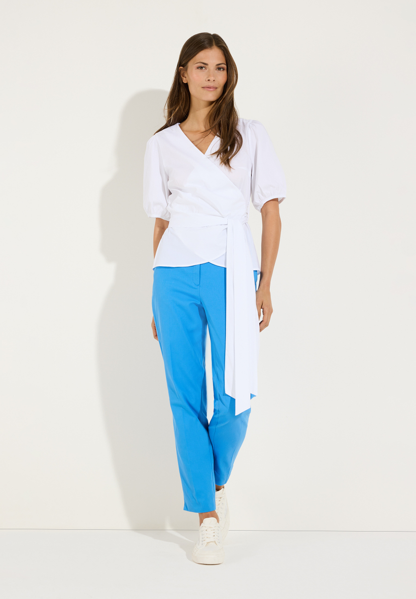 MORE & MORE Wickelbluse in Weiß mit Puffärmeln und Bindegürtel, kombiniert mit blauer Hose und weißen Sneakern. MORE & MORE Wickelbluse in Weiß mit Puffärmeln und Bindegürtel, kombiniert mit blauer Hose und weißen Sneakern.