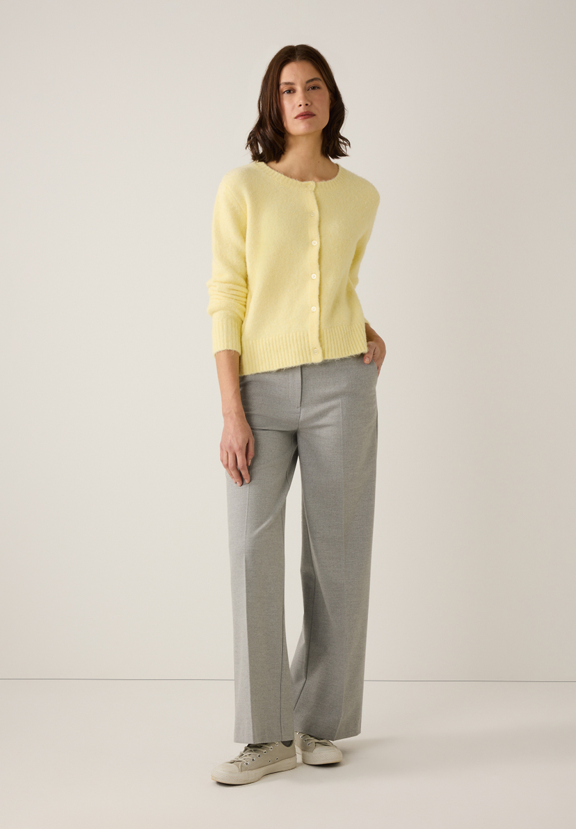 Eine Frau mit MORE & MORE Strickwaren-Oberteil, grauer Hose und Turnschuhen vor hellem Hintergrund. Eine Frau mit MORE & MORE Strickwaren-Oberteil, grauer Hose und Turnschuhen vor hellem Hintergrund.