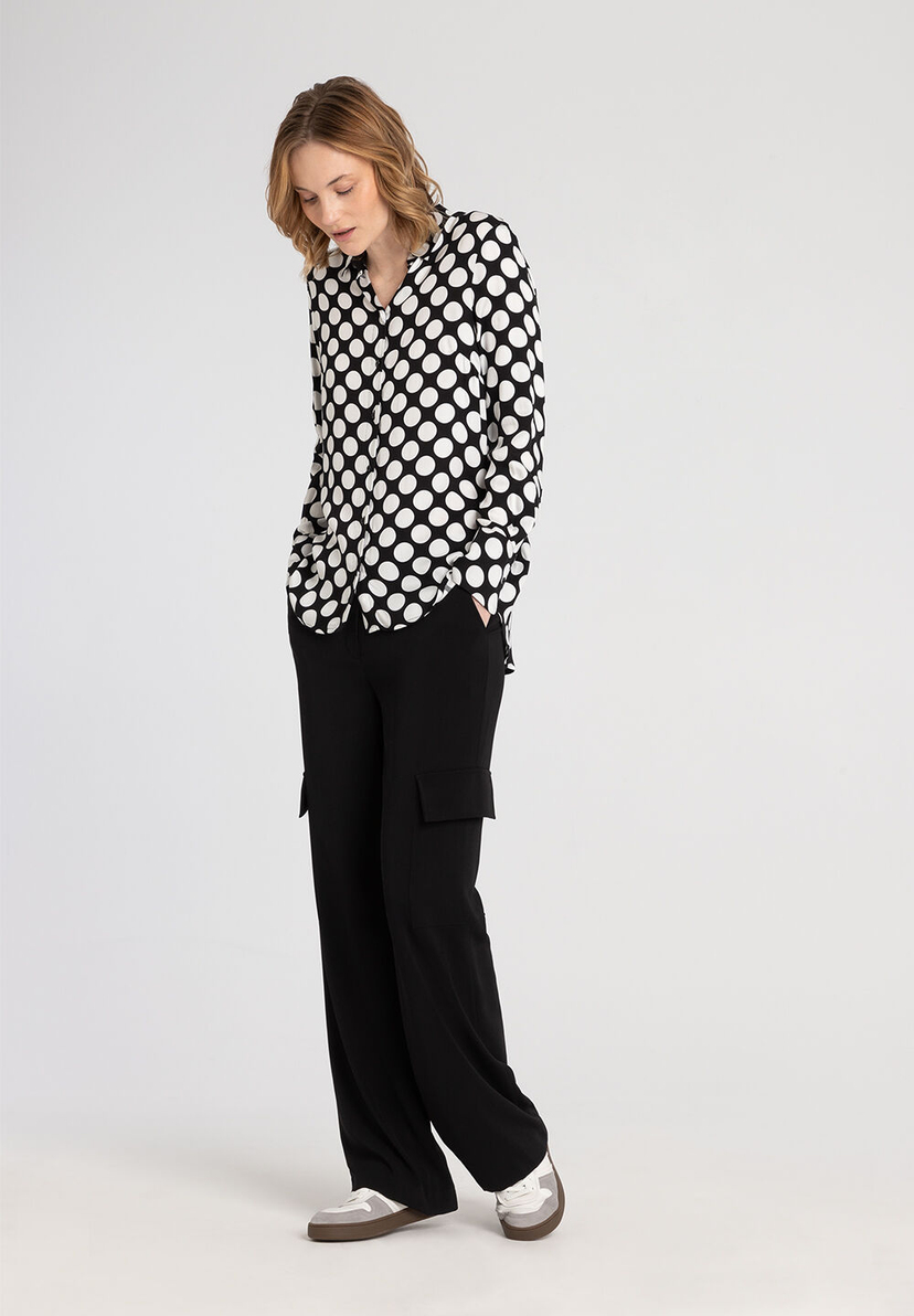 Eine Frau trägt ein Outfit von MORE & MORE: eine gepunktete Bluse und eine schwarze Hose. Eine Frau trägt ein Outfit von MORE & MORE: eine gepunktete Bluse und eine schwarze Hose.