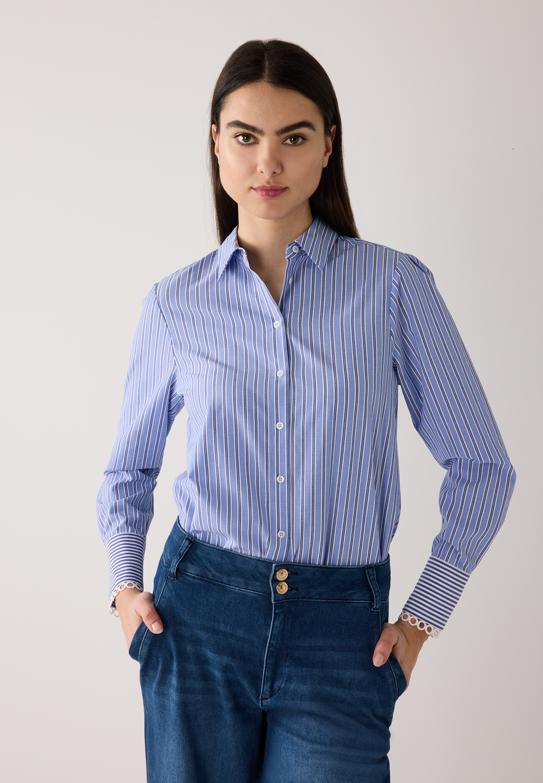 Eine Frau in einer blau-weiß gestreiften MORE & MORE Bluse aus Popeline und Jeans. Ihre Hände stecken in den Hosentaschen. Eine Frau in einer blau-weiß gestreiften MORE & MORE Bluse aus Popeline und Jeans. Ihre Hände stecken in den Hosentaschen.