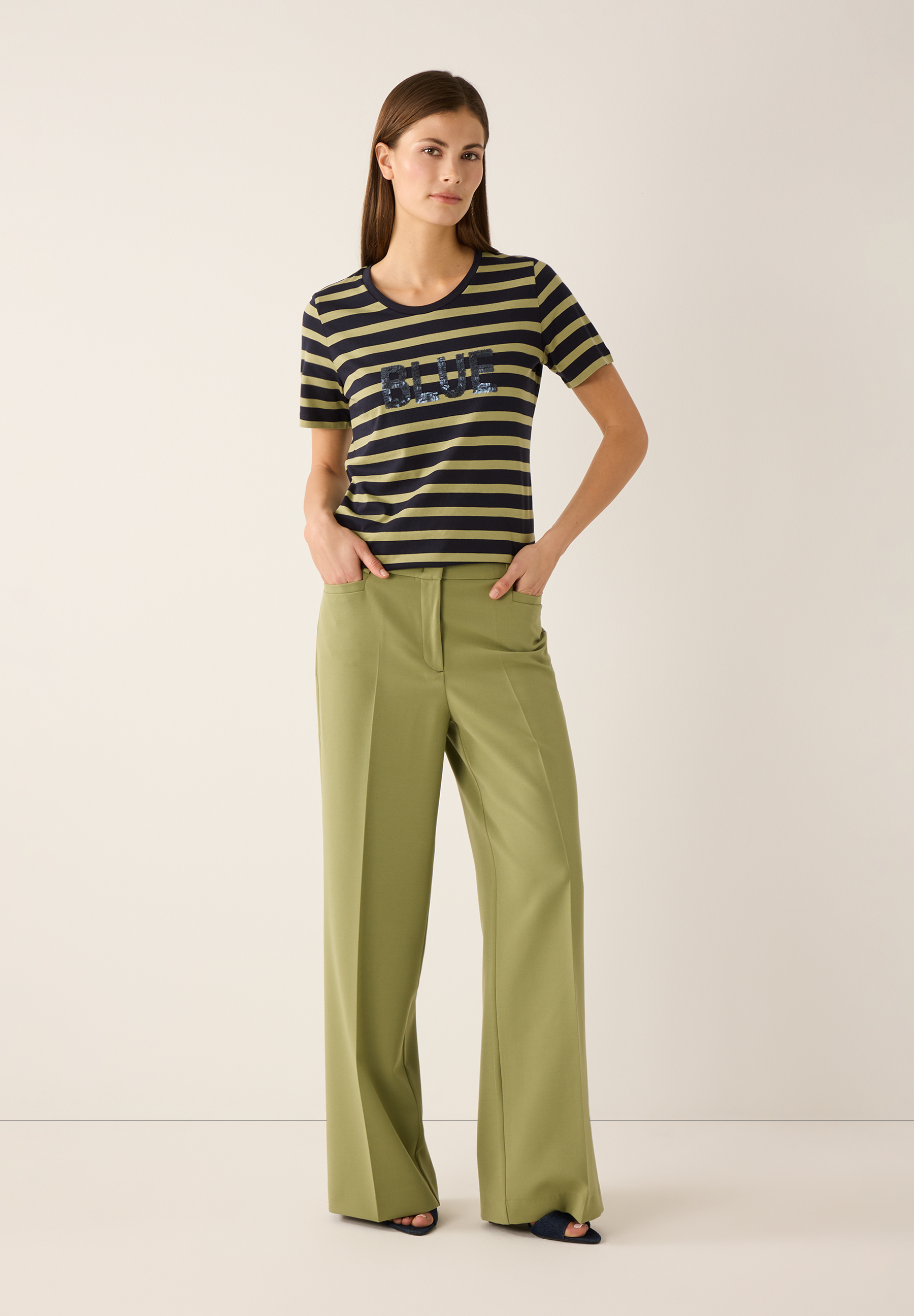 Eine Frau mit einem MORE & MORE T-Shirt mit blauem Schriftzug und grüner Hose. Eine Frau mit einem MORE & MORE T-Shirt mit blauem Schriftzug und grüner Hose.