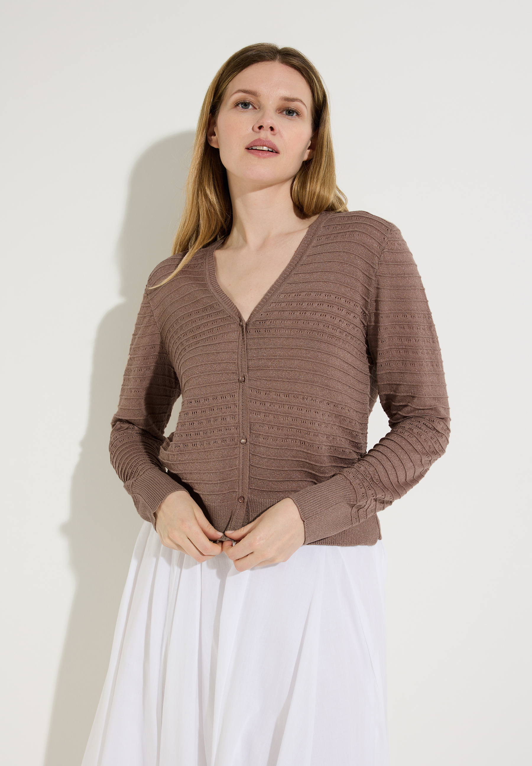 Eine Frau trägt einen braunen Strukturstrick-Cardigan von MORE & MORE und einen weißen Rock vor einem weißen Hintergrund. Eine Frau trägt einen braunen Strukturstrick-Cardigan von MORE & MORE und einen weißen Rock vor einem weißen Hintergrund.