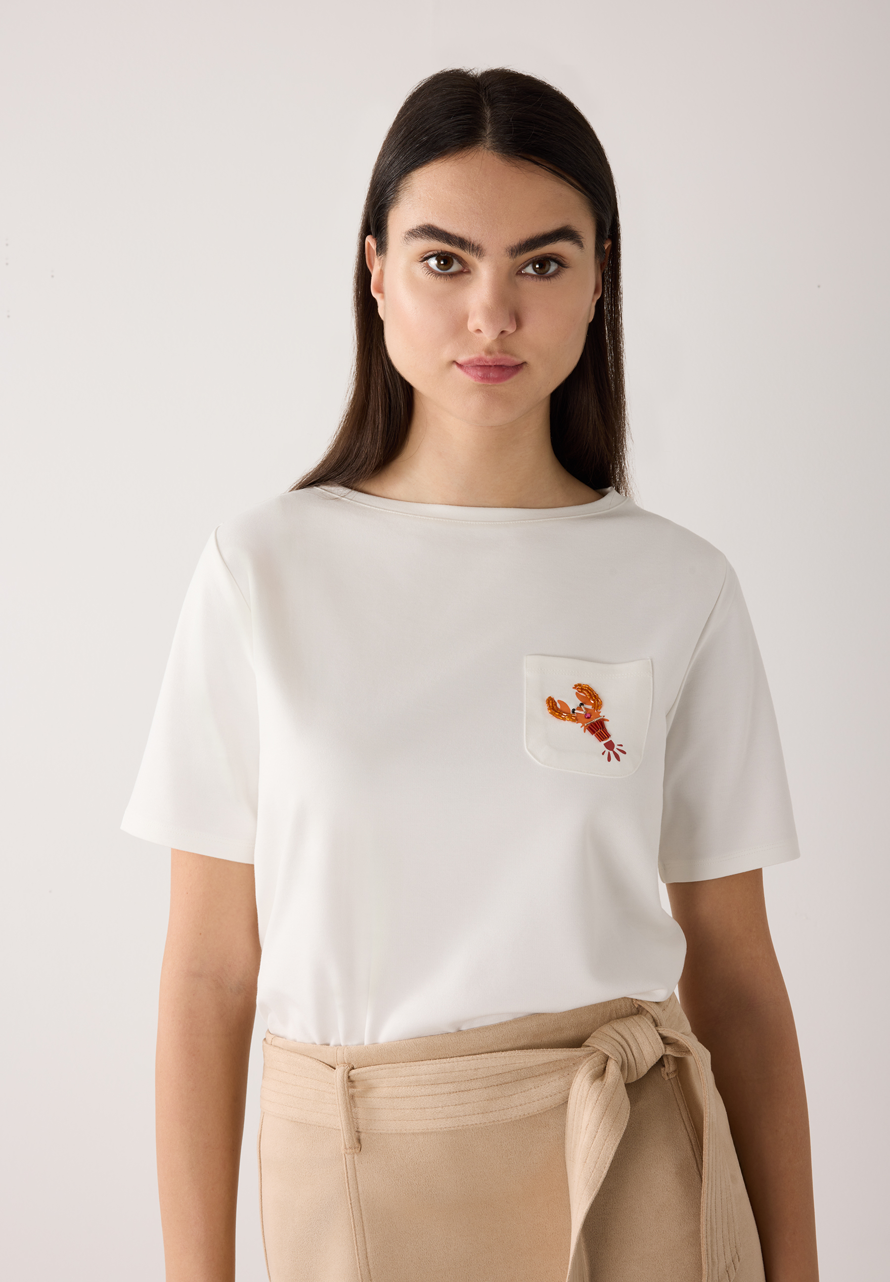 Eine Frau in einem weißen MORE & MORE T-Shirt mit Jersey-Material und einer Hummer-Applikation auf der Tasche.