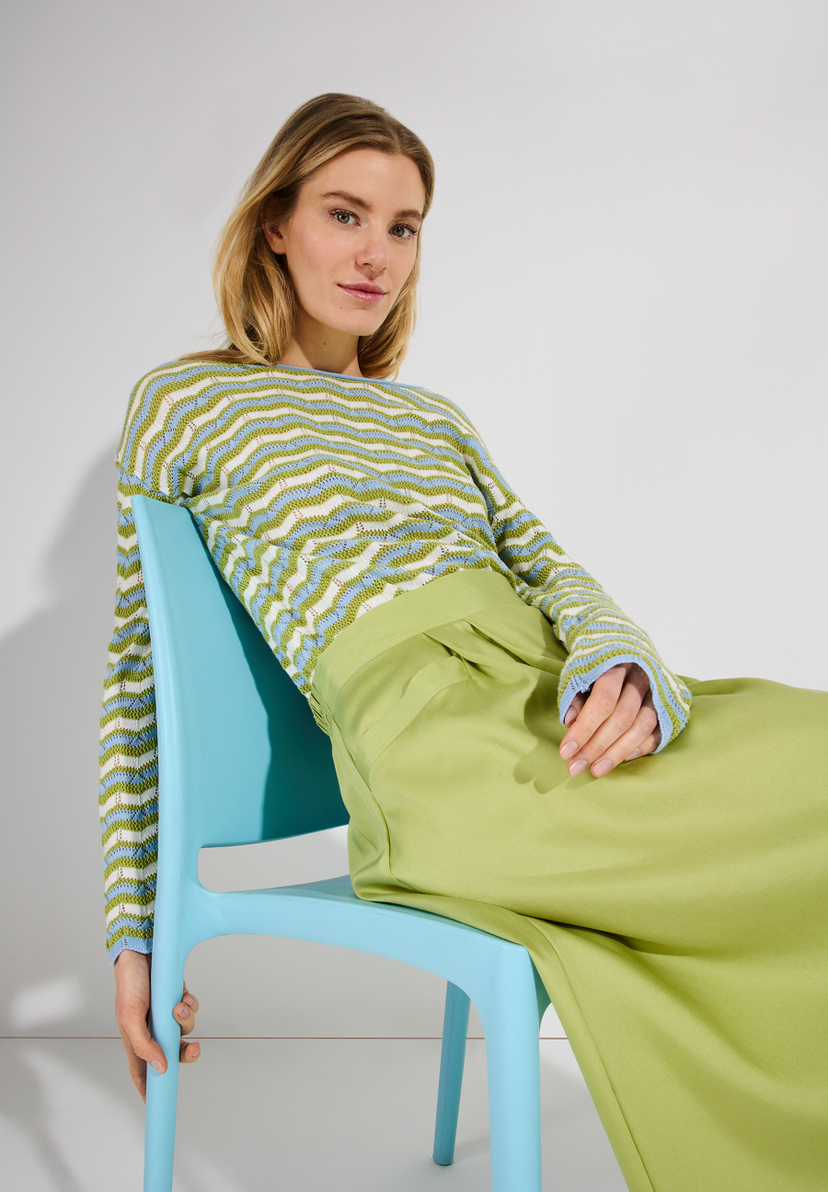 Eine Frau sitzt auf einem blauen Stuhl und trägt einen Rock von MORE & MORE aus Satin. Eine Frau sitzt auf einem blauen Stuhl und trägt einen Rock von MORE & MORE aus Satin.