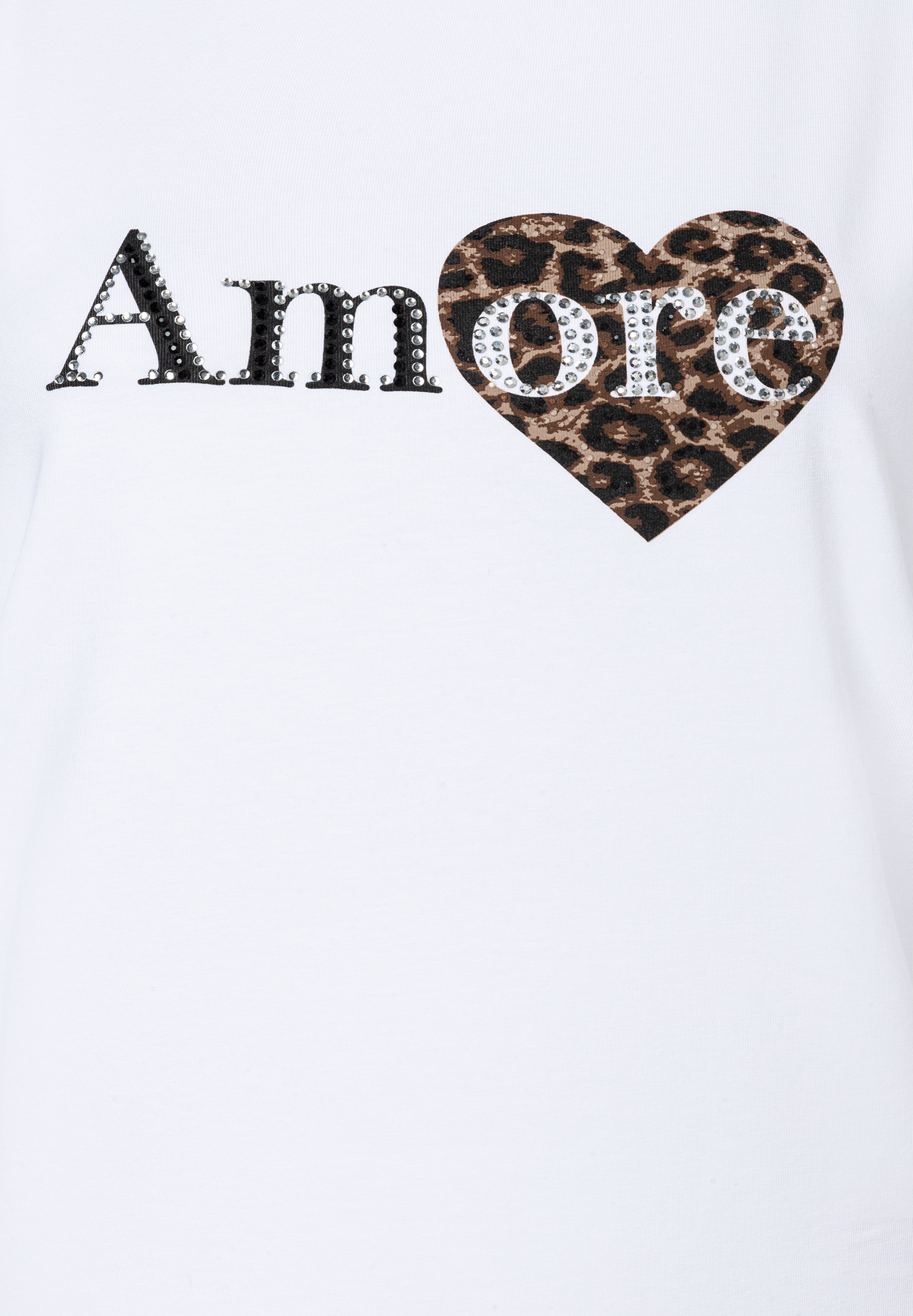 Ausschnitt eines weißen MORE & MORE Oberteils mit „Amore“-Print. Funkelnde Akzente. Ausschnitt eines weißen MORE & MORE Oberteils mit „Amore“-Print. Funkelnde Akzente.