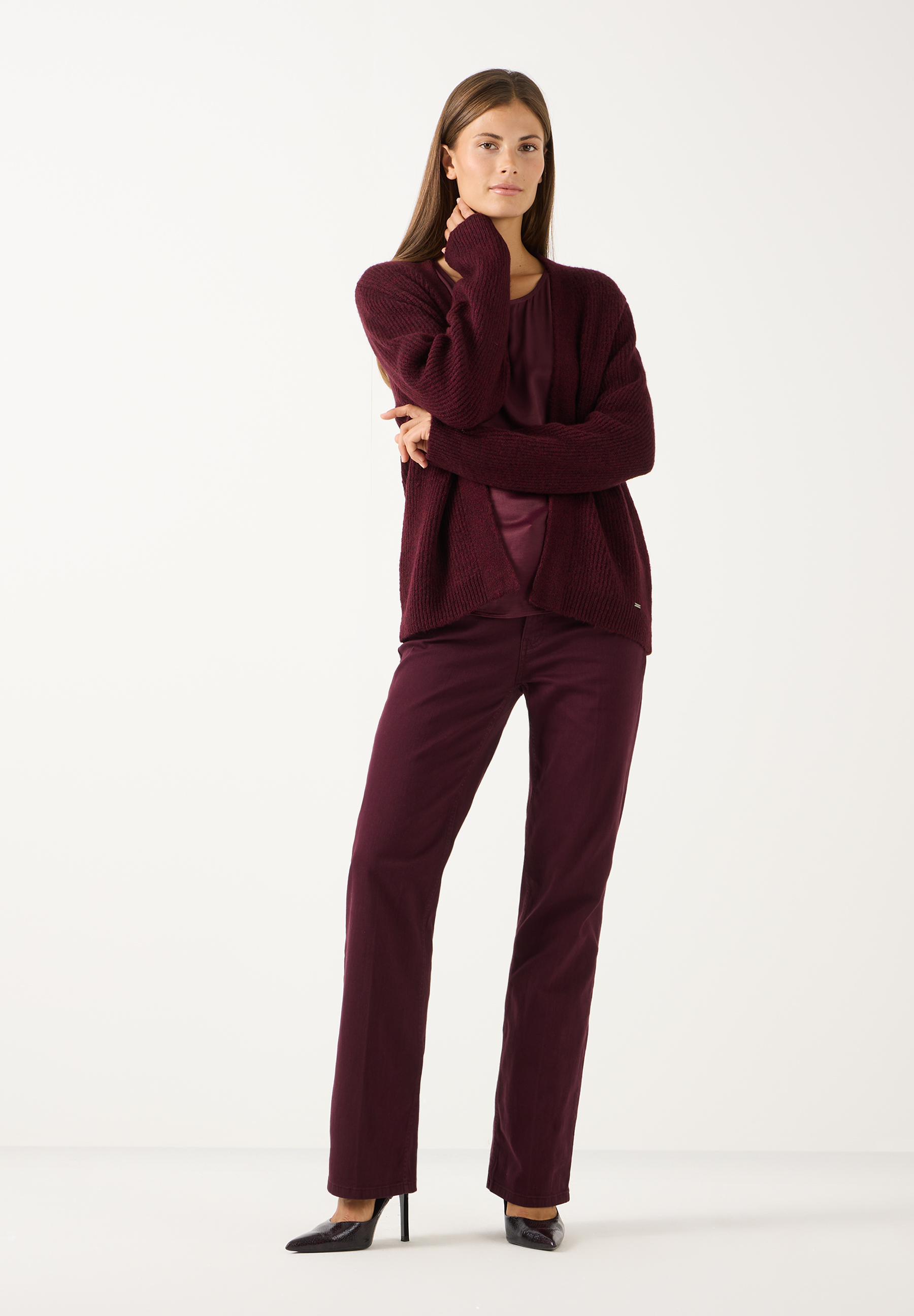 MORE & MORE Jeans: Das Model trägt eine bordeauxrote Jeans und einen passenden Oberteil mit Strickjacke. MORE & MORE Jeans: Das Model trägt eine bordeauxrote Jeans und einen passenden Oberteil mit Strickjacke.