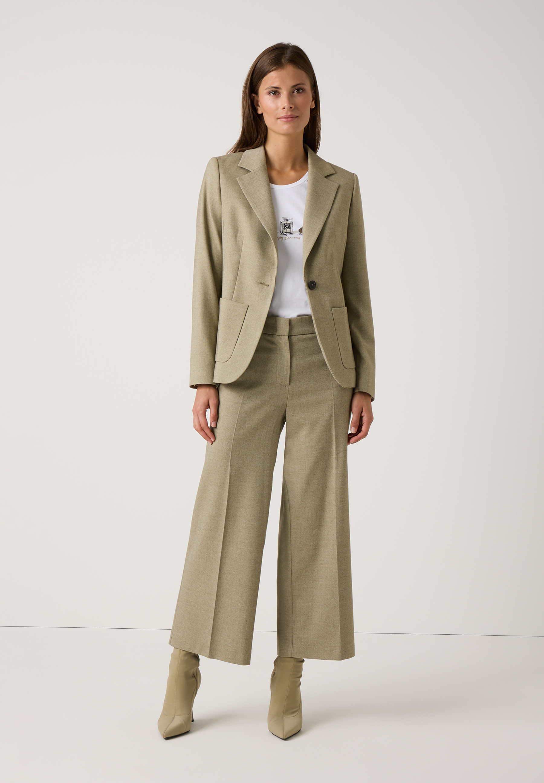 Eine Frau in einem olivgrünen Hosenanzug und MORE & MORE Oberteil mit Jersey-Materialkonstruktion. Eine Frau in einem olivgrünen Hosenanzug und MORE & MORE Oberteil mit Jersey-Materialkonstruktion.