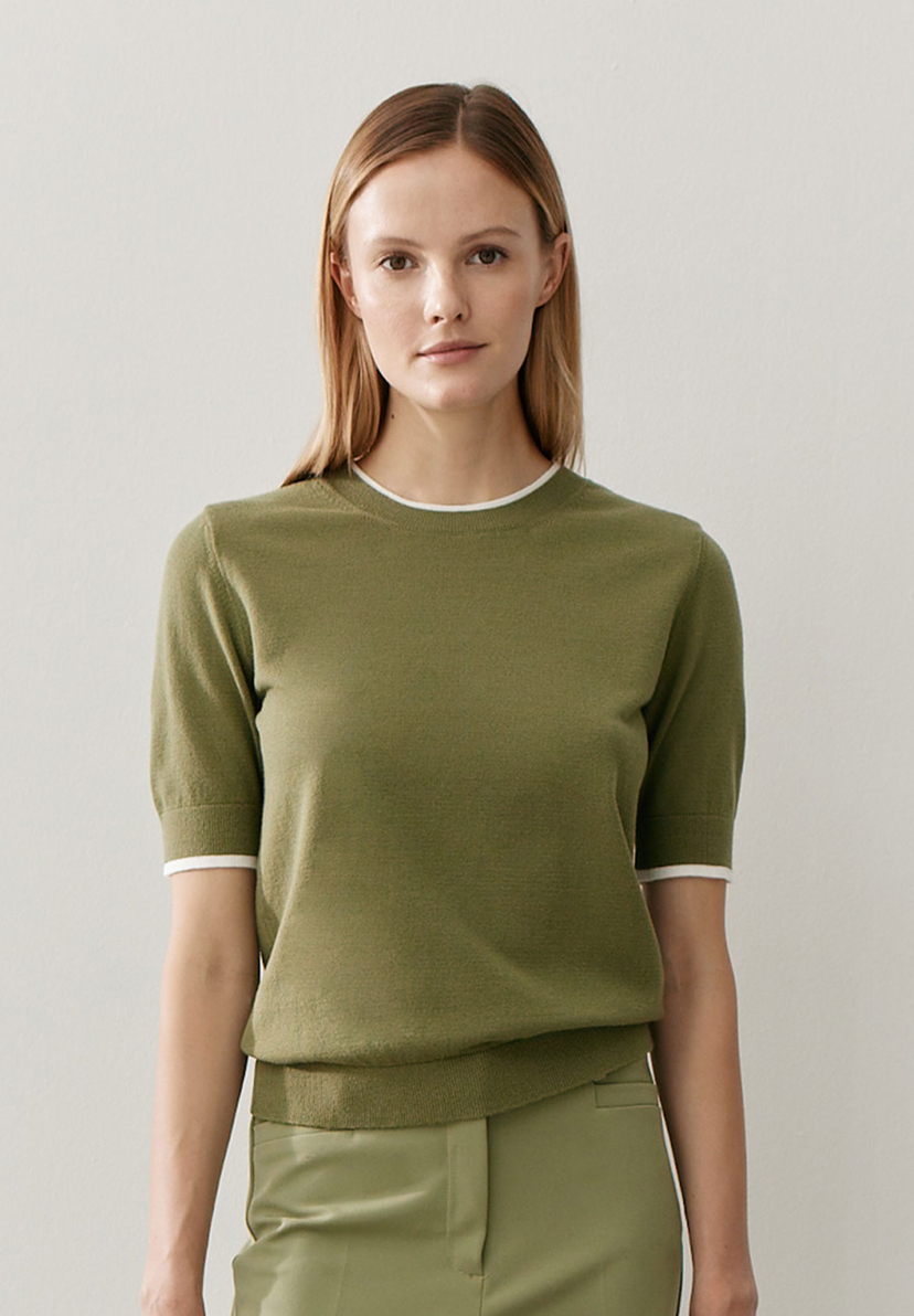 Eine Frau mit einem olivgrünen Feinstrick-Oberteil von MORE & MORE. Der Pullover hat weiße Akzente an Ärmeln und Kragen. Eine Frau mit einem olivgrünen Feinstrick-Oberteil von MORE & MORE. Der Pullover hat weiße Akzente an Ärmeln und Kragen.