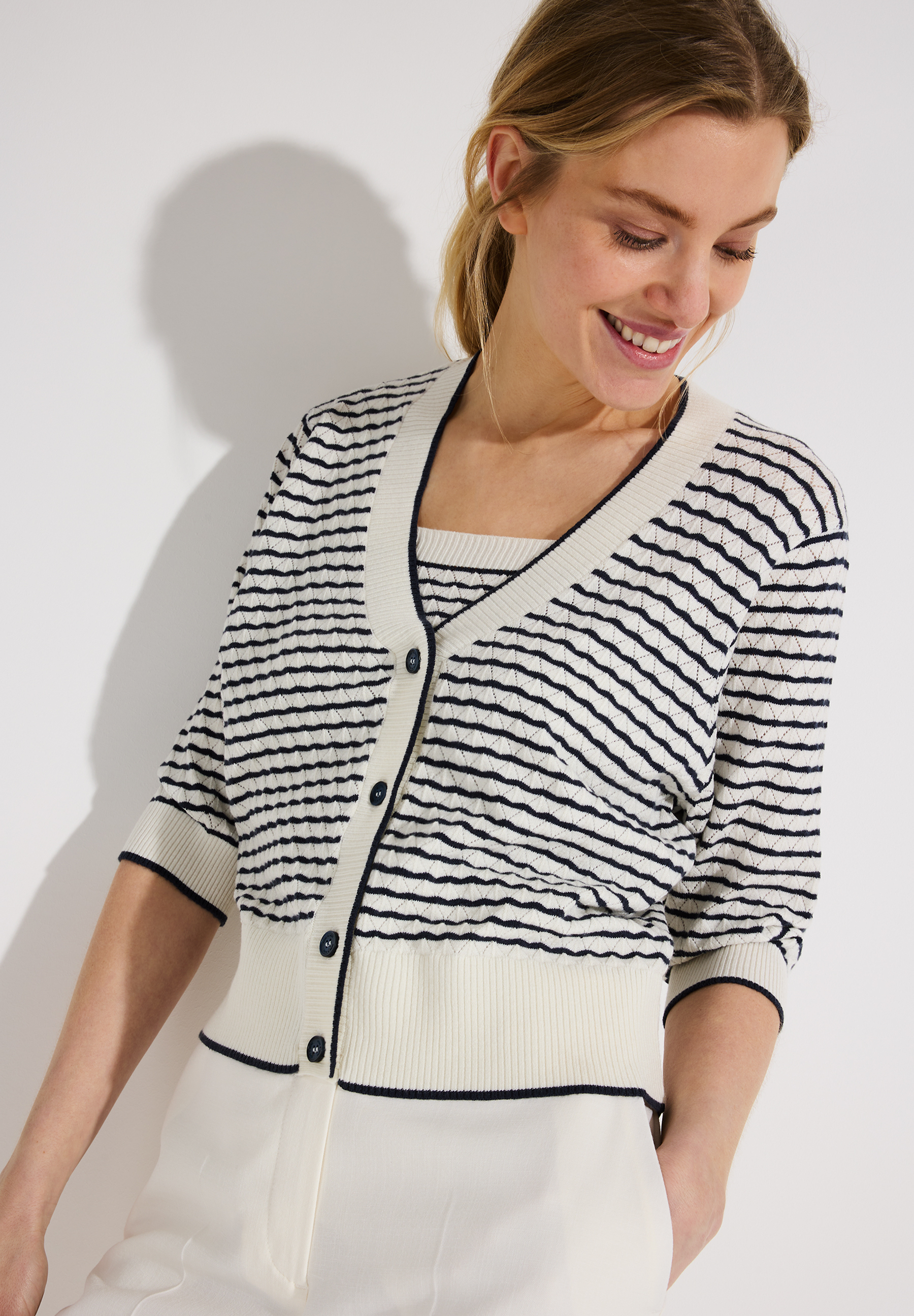 Eine Frau trägt einen MORE & MORE Strickpullover mit Streifen. Sie lächelt und hat die Hände in den Hosentaschen. Eine Frau trägt einen MORE & MORE Strickpullover mit Streifen. Sie lächelt und hat die Hände in den Hosentaschen.
