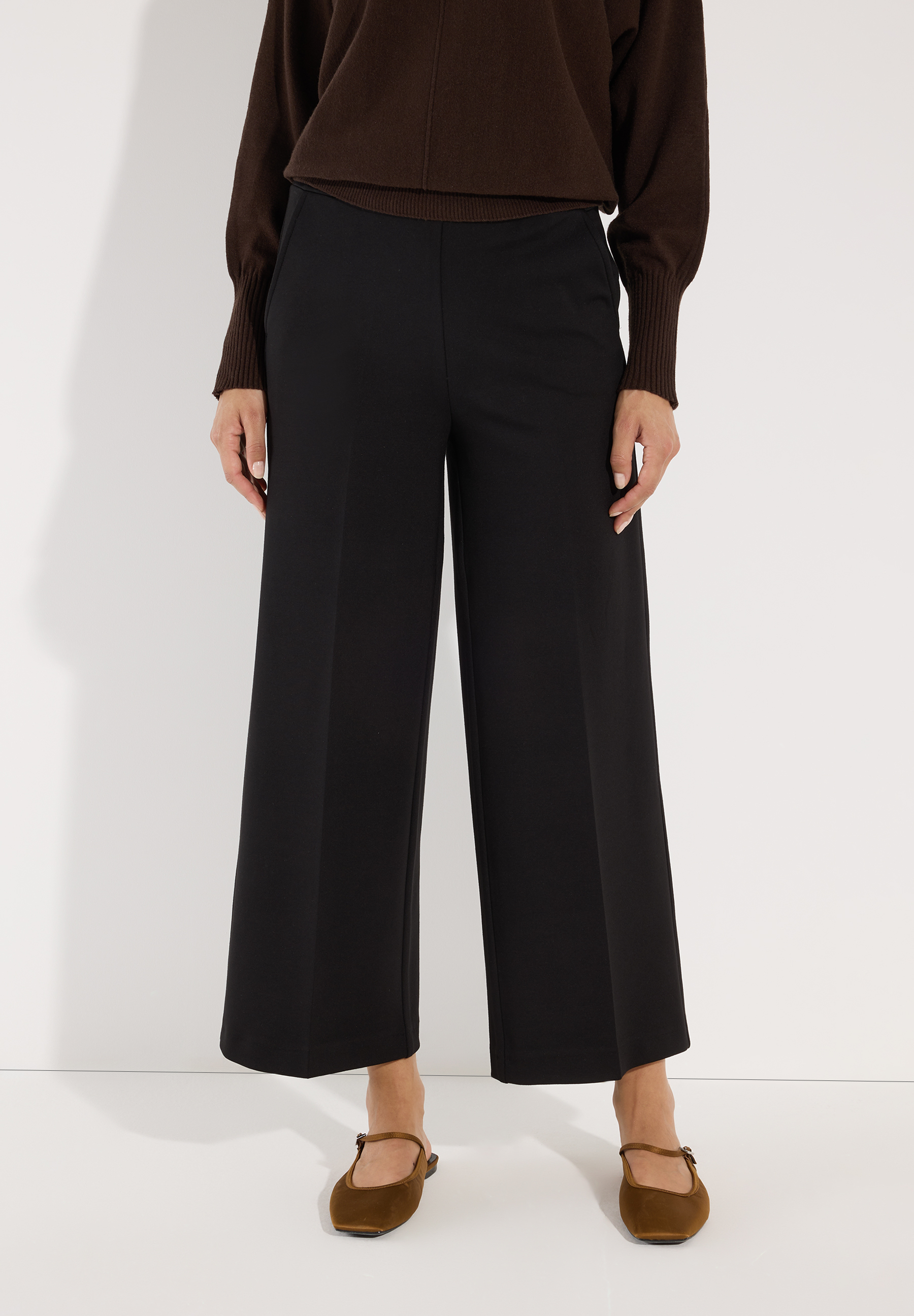 MORE & MORE schwarze Cropped-Culottes. Das Model trägt dazu einen braunen Strickpullover und braune Mary-Jane-Schuhe.