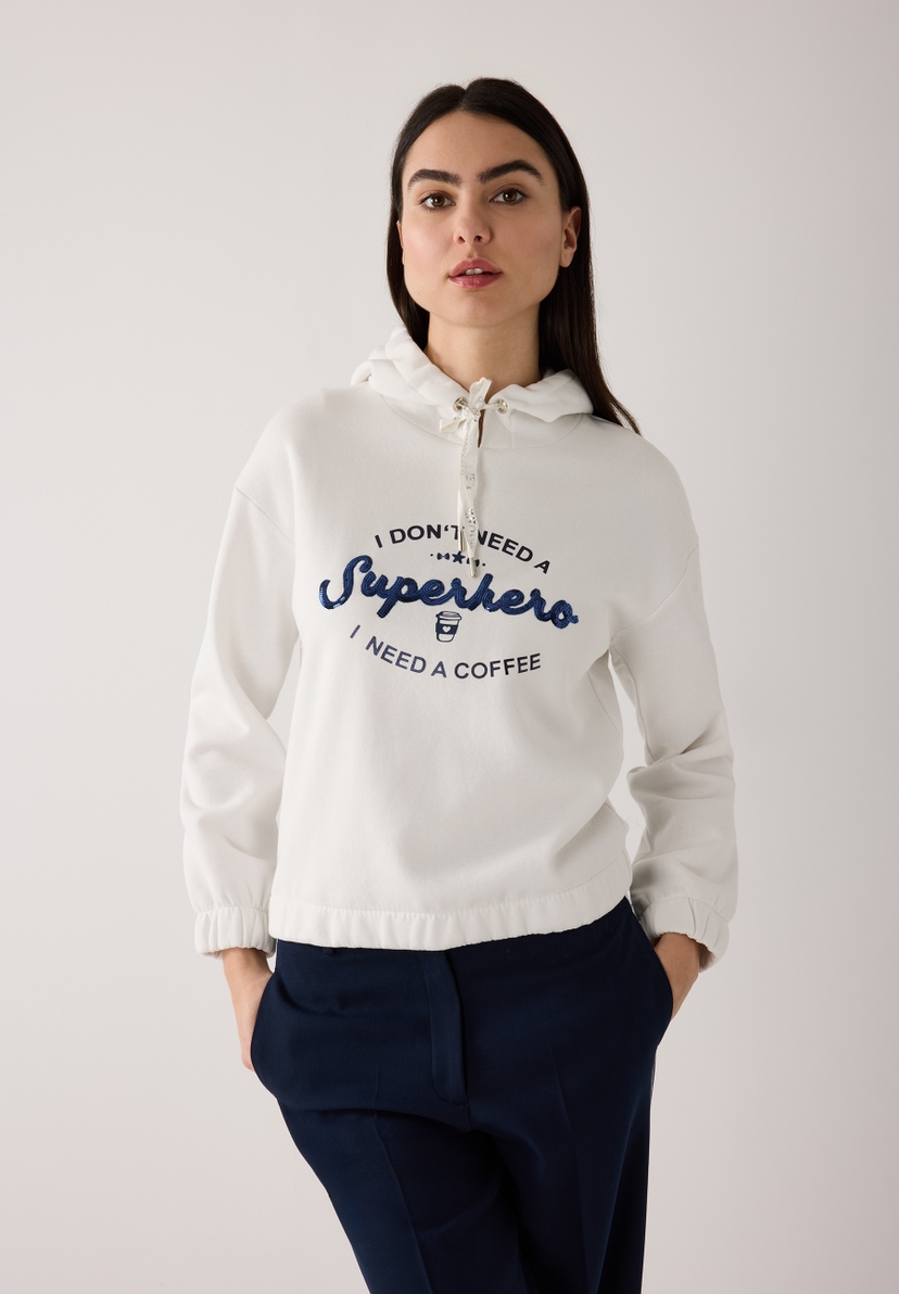 Eine Frau trägt ein MORE & MORE Sweatshirt mit der Aufschrift: 'I don't need a Superhero, I need a coffee'. Eine Frau trägt ein MORE & MORE Sweatshirt mit der Aufschrift: 'I don't need a Superhero, I need a coffee'.