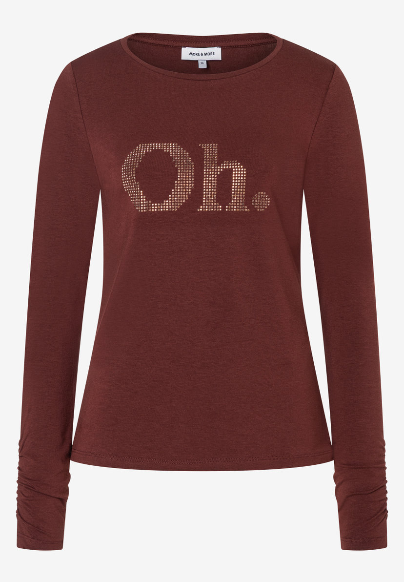 Ein Shirt von MORE & MORE in Rostrot mit langem Arm. Auf der Brust der Schriftzug "Oh." in goldenen Pailletten. Ein Shirt von MORE & MORE in Rostrot mit langem Arm. Auf der Brust der Schriftzug "Oh." in goldenen Pailletten.