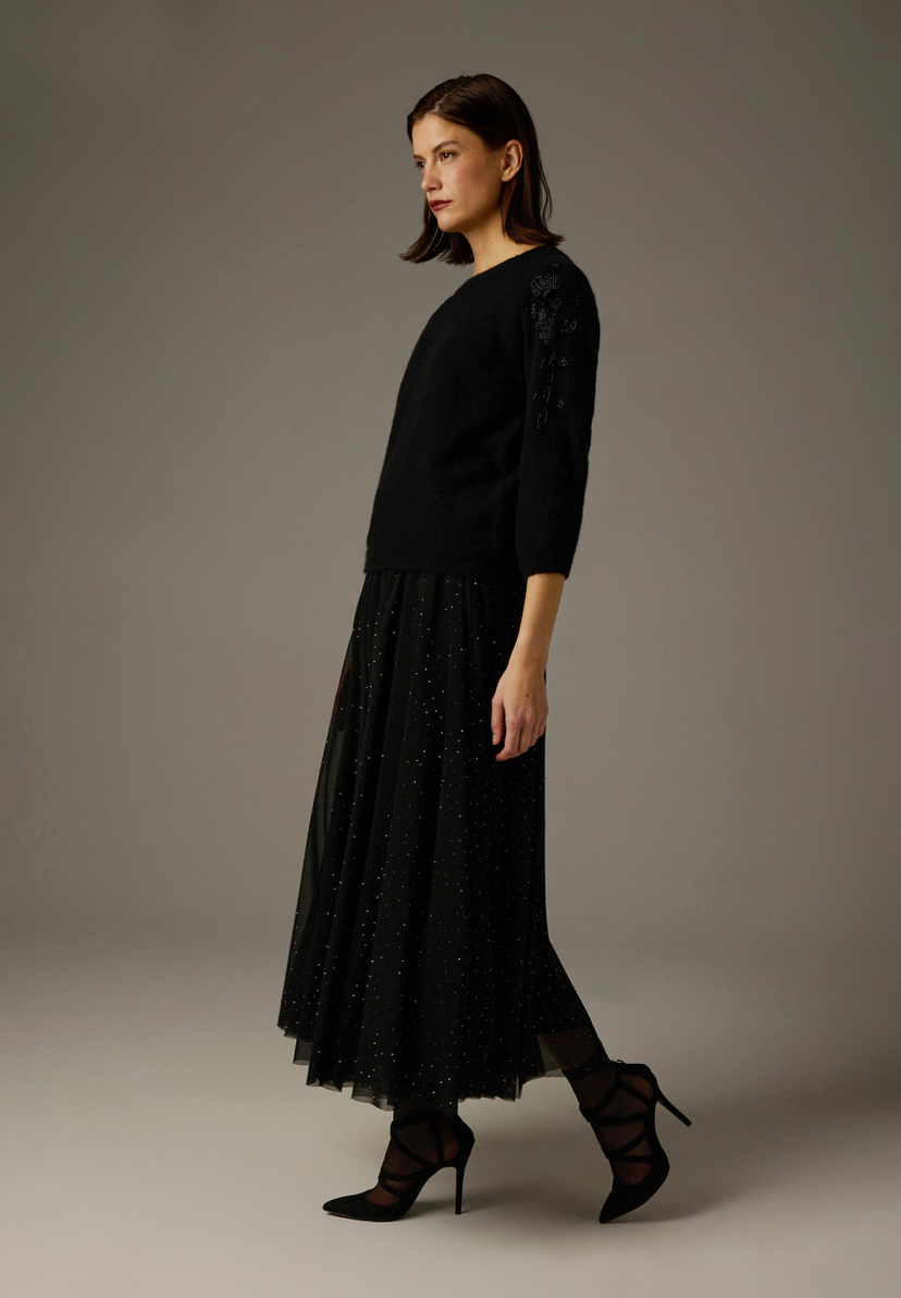Ein schwarzer MORE & MORE Strick-Pullover mit floralem Muster am Ärmel, kombiniert mit einem langen, glitzernden Rock. Ein schwarzer MORE & MORE Strick-Pullover mit floralem Muster am Ärmel, kombiniert mit einem langen, glitzernden Rock.