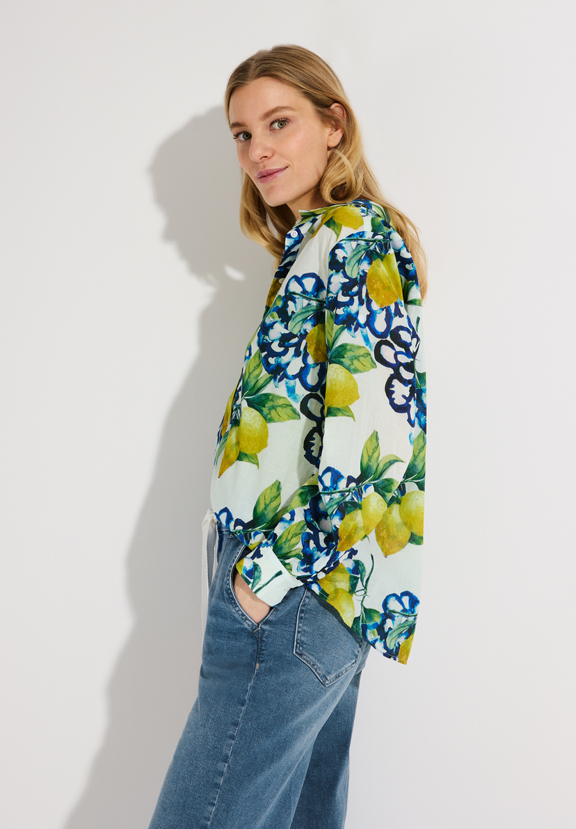 Eine Frau mit einer Bluse von MORE & MORE mit Zitronen- und Blumenmuster und Jeans. Eine Frau mit einer Bluse von MORE & MORE mit Zitronen- und Blumenmuster und Jeans.