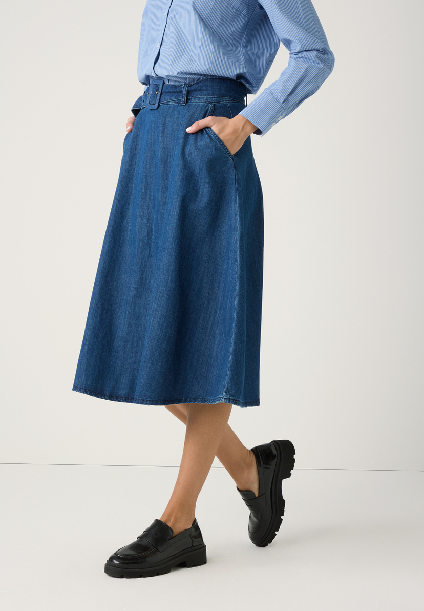 Ein Model präsentiert einen Jeansrock von MORE & MORE mit angenehmem Tragekomfort, kombiniert mit einer blau gestreiften Bluse und schwarzen Loafers. Ein Model präsentiert einen Jeansrock von MORE & MORE mit angenehmem Tragekomfort, kombiniert mit einer blau gestreiften Bluse und schwarzen Loafers.