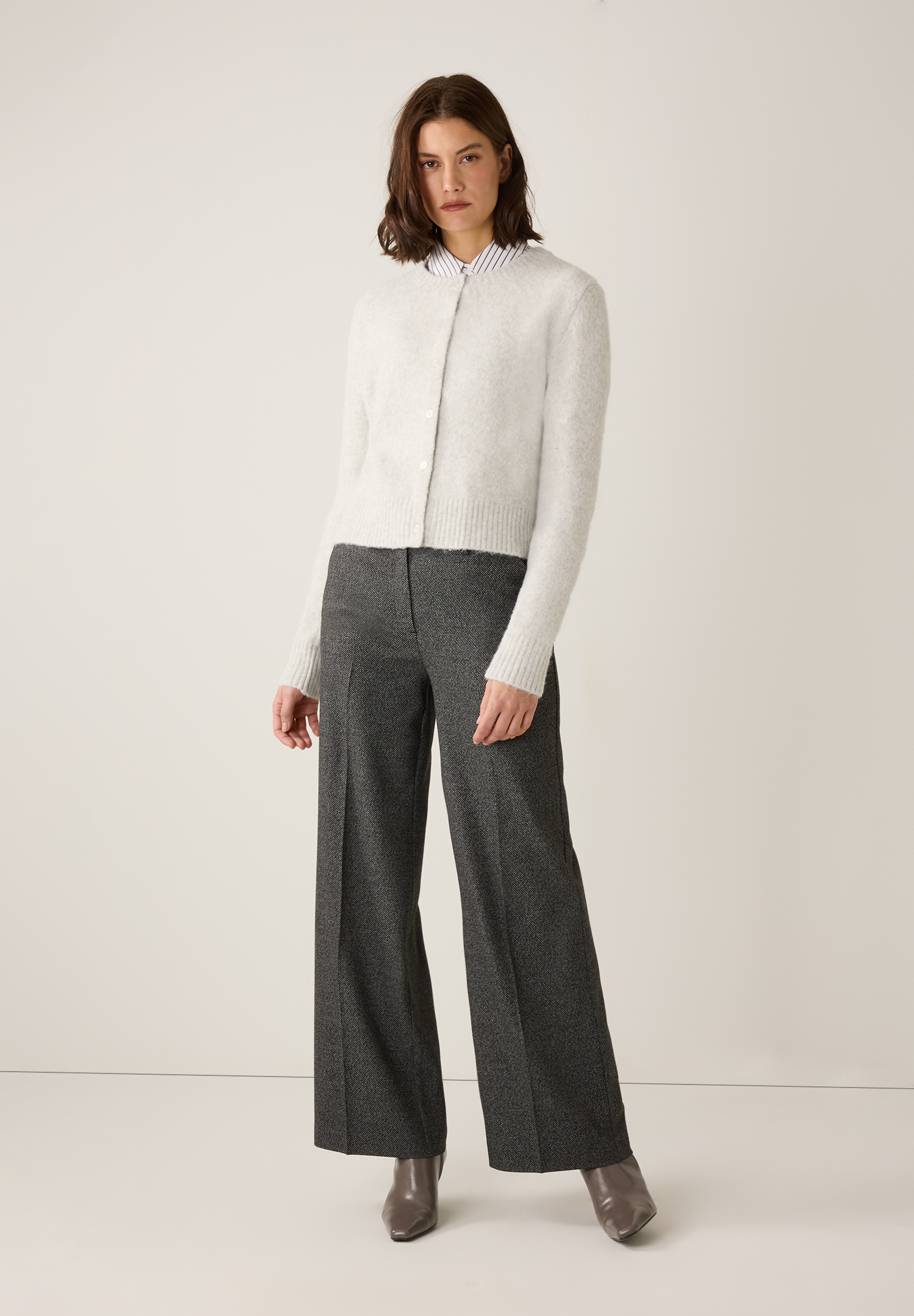Eine Frau trägt einen MORE & MORE Cardigan, eine gestreifte Bluse und eine graue Hose. Eine Frau trägt einen MORE & MORE Cardigan, eine gestreifte Bluse und eine graue Hose.