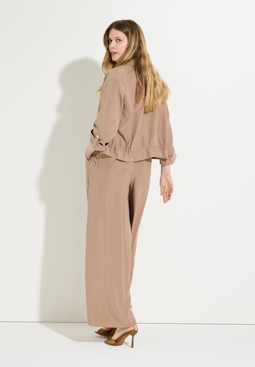 Eine Frau in MORE & MORE Oberteilen und Hose blickt über die Schulter. Eine Frau in MORE & MORE Oberteilen und Hose blickt über die Schulter.