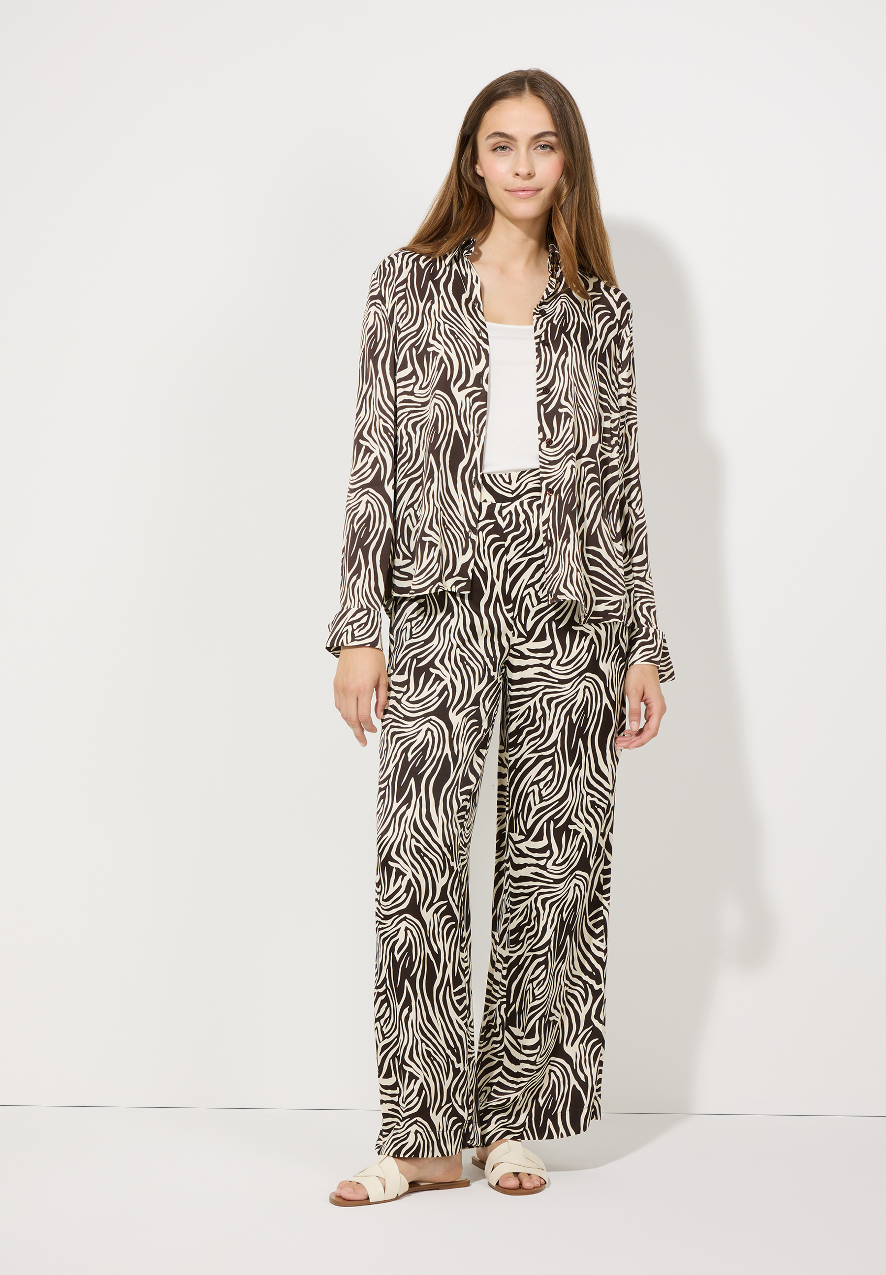 Eine Frau im MORE & MORE Viskose-Oberteil mit Zebra-Muster und passender Hose, die für angenehmen Tragekomfort sorgt. Eine Frau im MORE & MORE Viskose-Oberteil mit Zebra-Muster und passender Hose, die für angenehmen Tragekomfort sorgt.