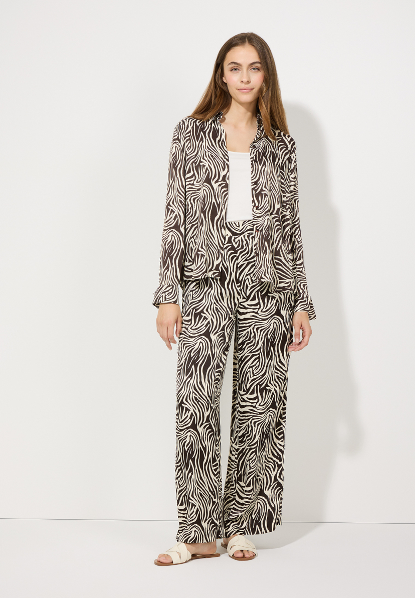 Eine Frau im MORE & MORE Viskose-Oberteil mit Zebra-Muster und passender Hose, die für angenehmen Tragekomfort sorgt. Eine Frau im MORE & MORE Viskose-Oberteil mit Zebra-Muster und passender Hose, die für angenehmen Tragekomfort sorgt.