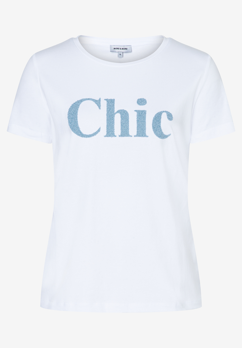 Ein weißes MORE & MORE T-Shirt mit dem blauen, glitzernden Schriftzug "Chic" auf der Vorderseite. Ein weißes MORE & MORE T-Shirt mit dem blauen, glitzernden Schriftzug "Chic" auf der Vorderseite.