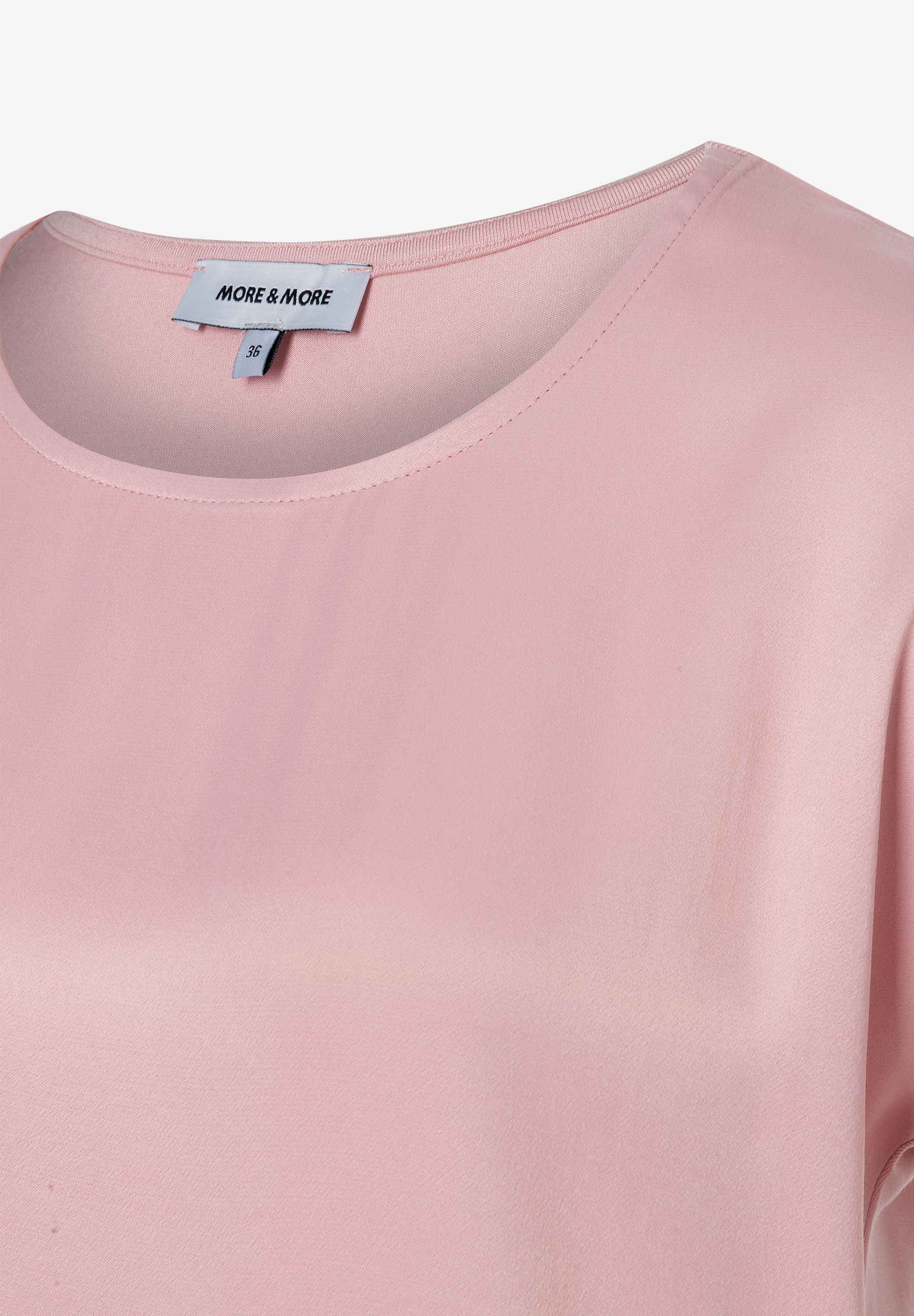 Nahaufnahme eines MORE & MORE Oberteils mit Rundhalsausschnitt in zartem Rosa. Ein Etikett ist sichtbar.