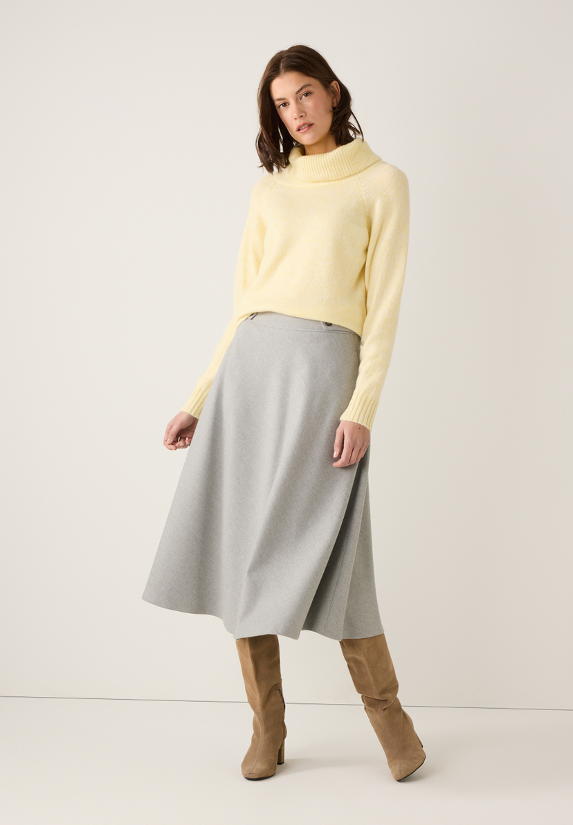 Eine Frau in MORE & MORE Strickmode: gelber Pullover, grauer Rock und braune Stiefel. Eine Frau in MORE & MORE Strickmode: gelber Pullover, grauer Rock und braune Stiefel.